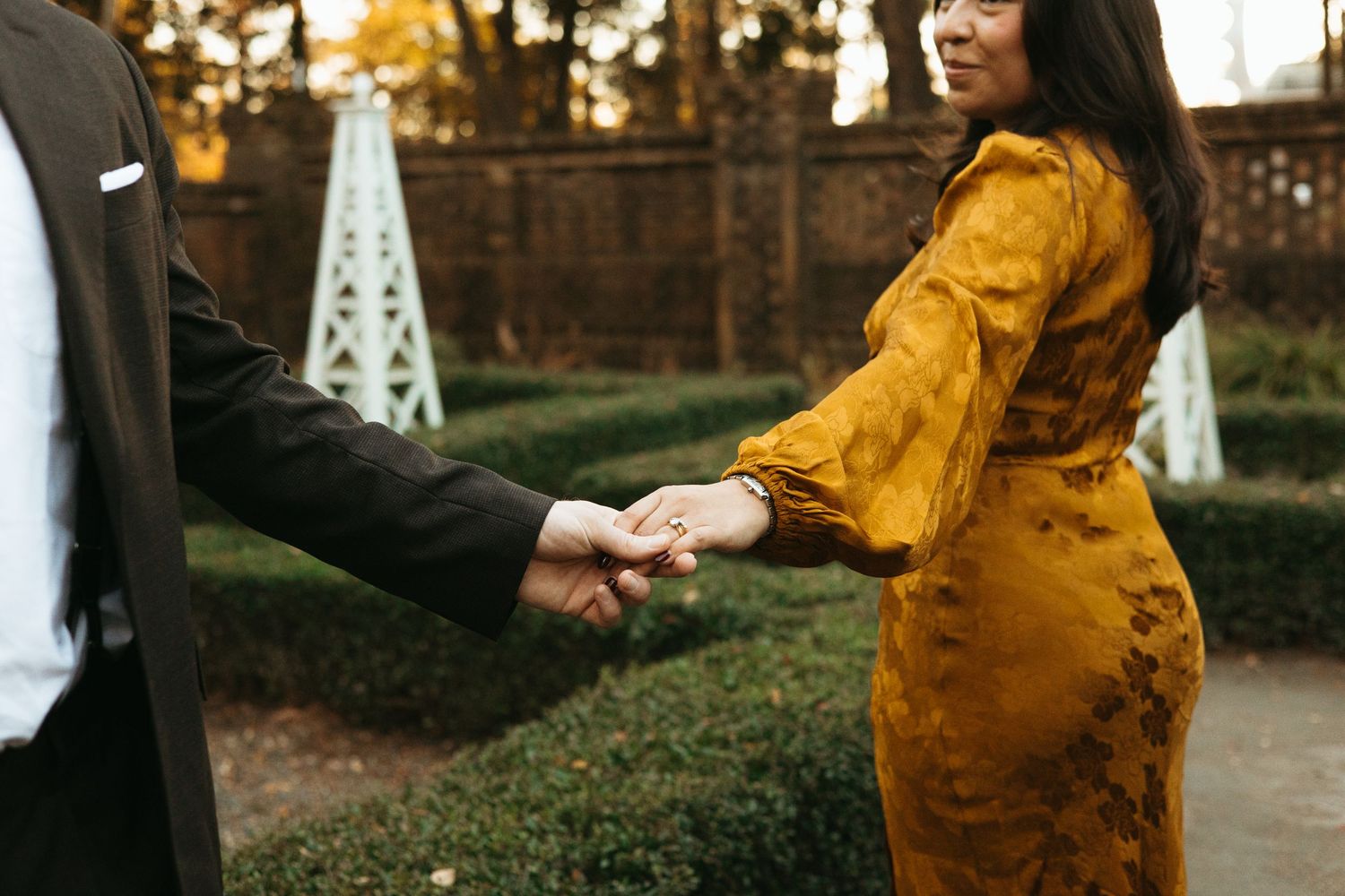 Close-up of couple holding hands, woman wearing elegant mustard yellow velvet dress outdoors.
