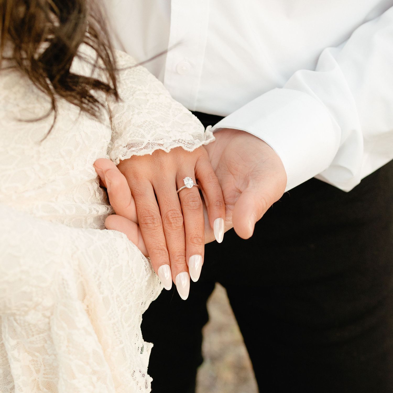 Close-up of bride's hand showing diamond engagement ring resting on groom's hand.