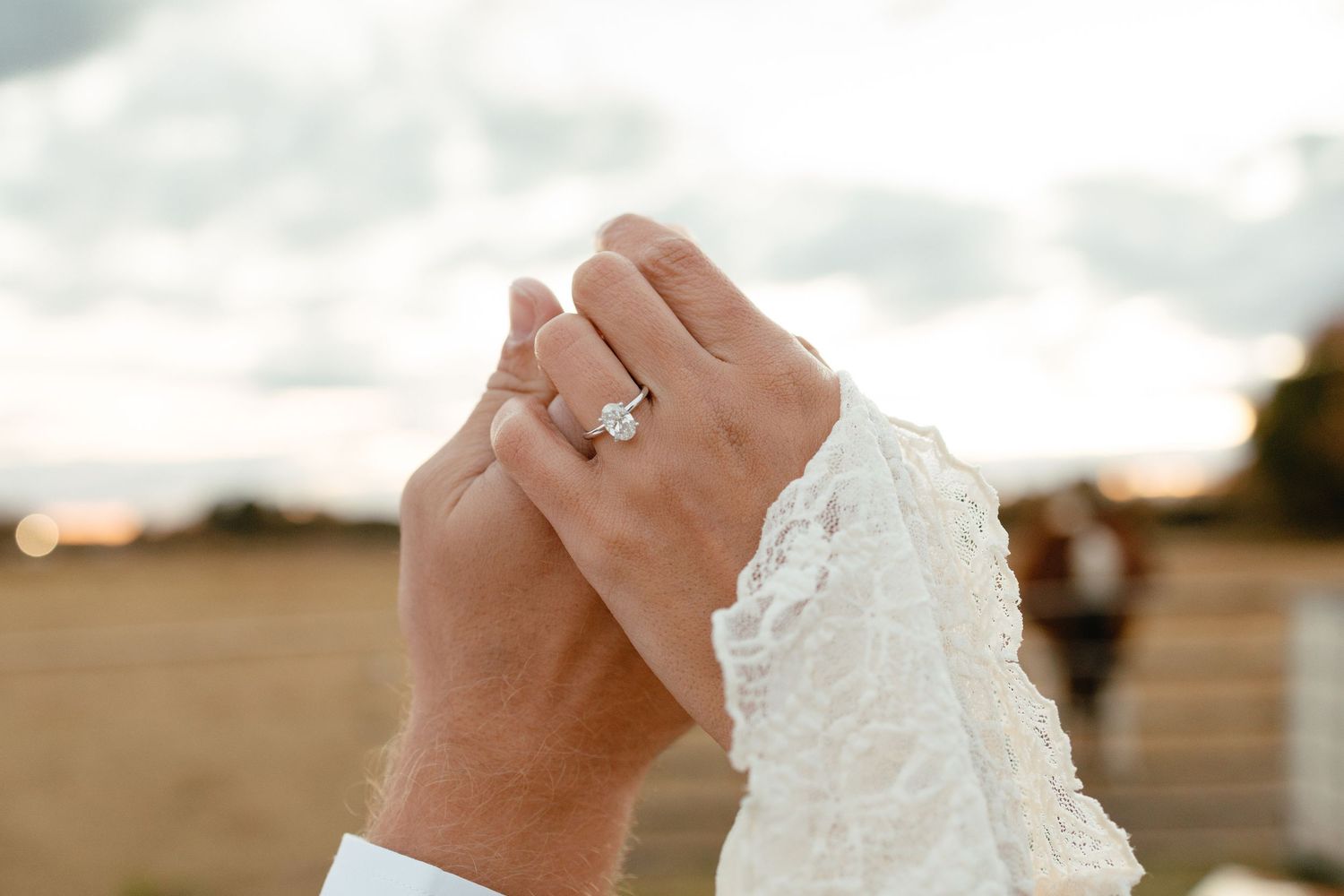 Close-up of bride's elegant diamond engagement ring on wedding day with lace dress detail.
