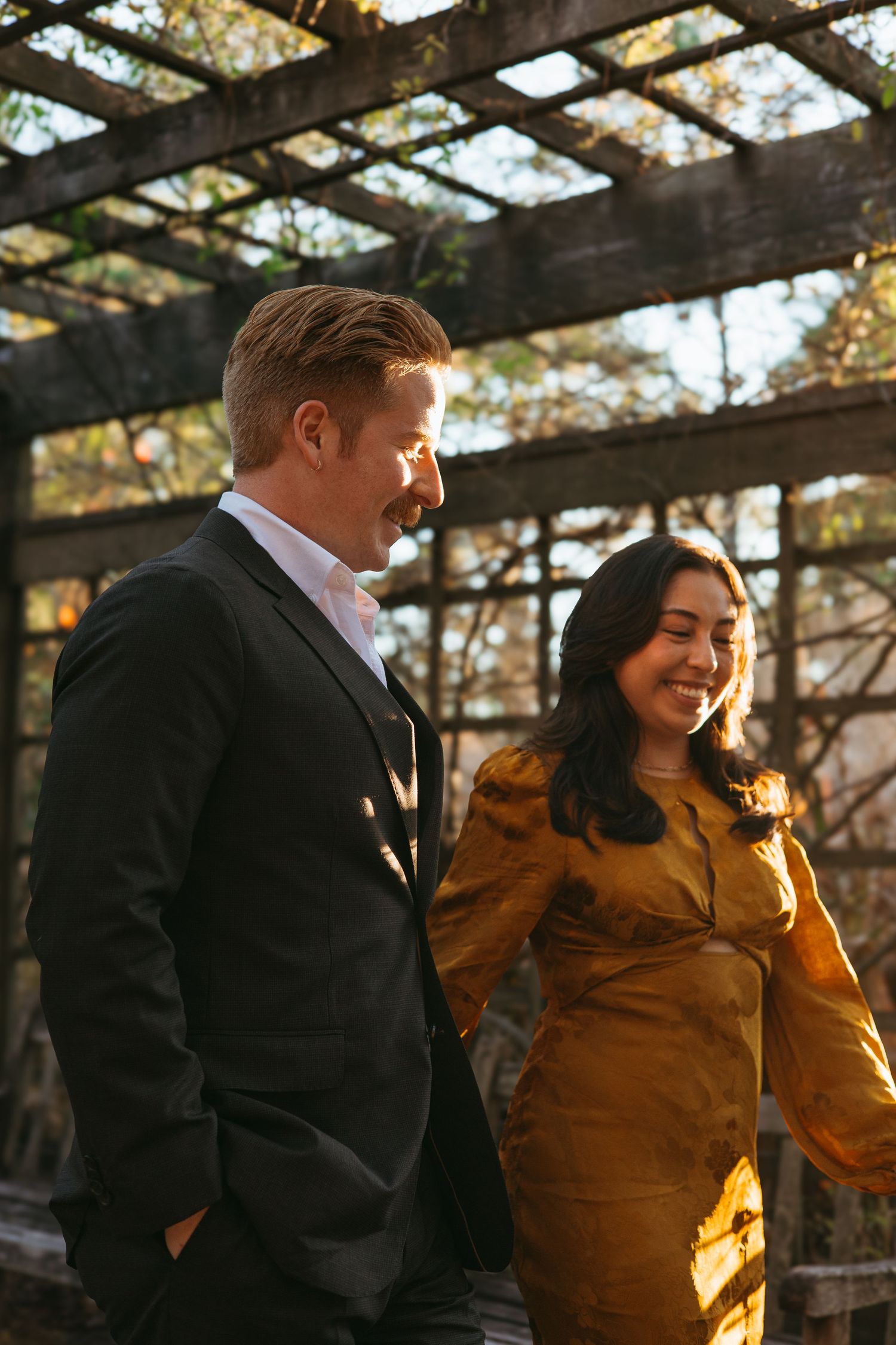 Laughing couple strolling under a pergola bathed in warm golden sunlight.