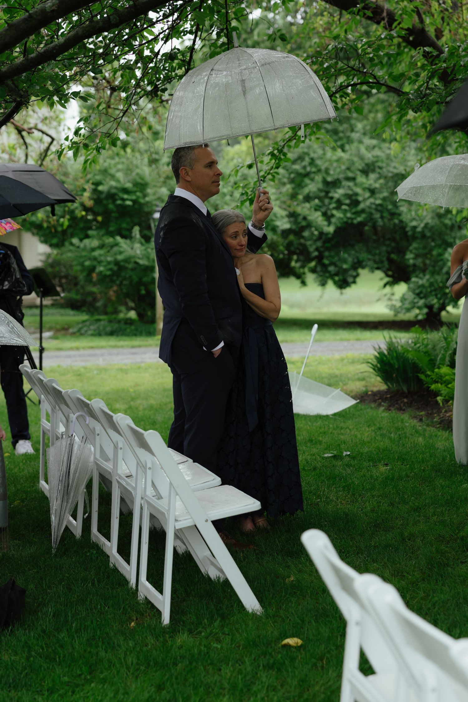 Couple standing under a clear bubble umbrella at an outdoor wedding ceremony on a rainy day.