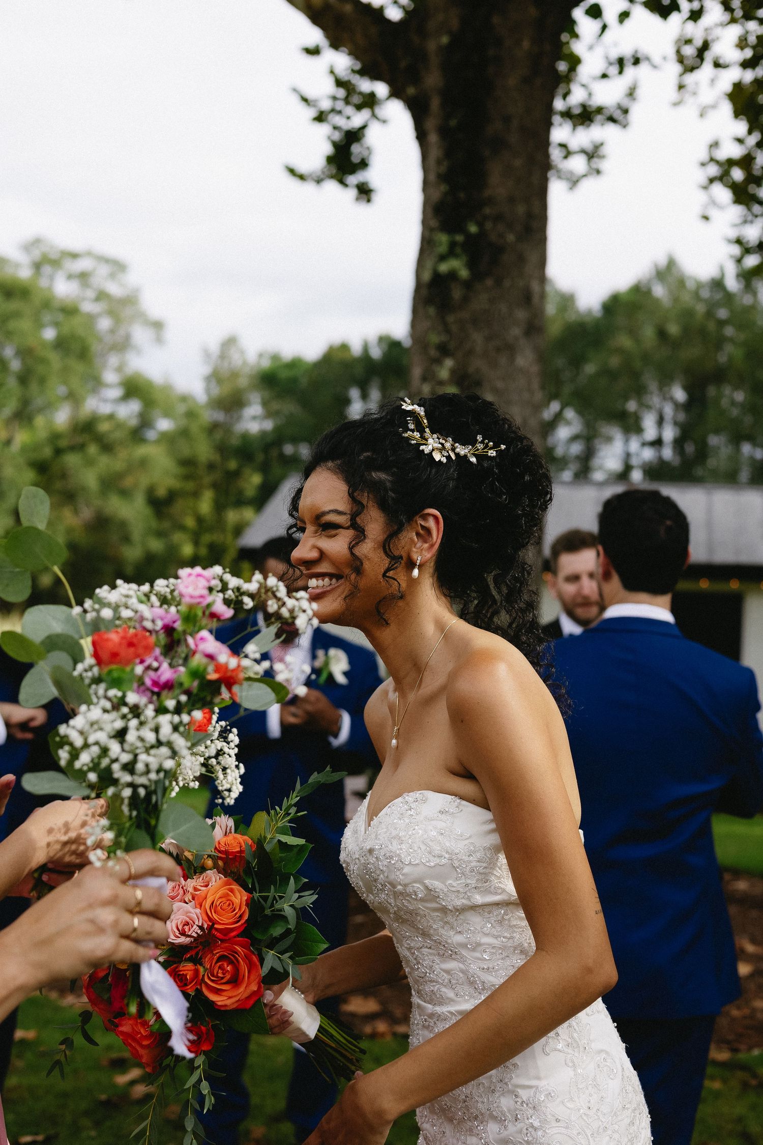 Radiant bride in strapless lace gown smiling joyfully while holding a vibrant colorful wedding bouquet.