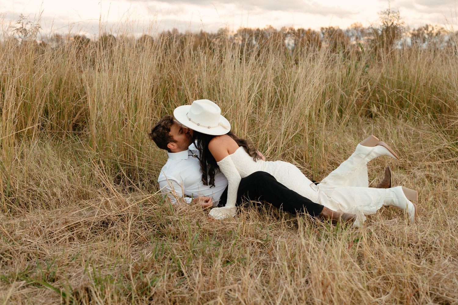 Bride and groom playfully embracing and laughing together in a golden field during outdoor wedding photos.