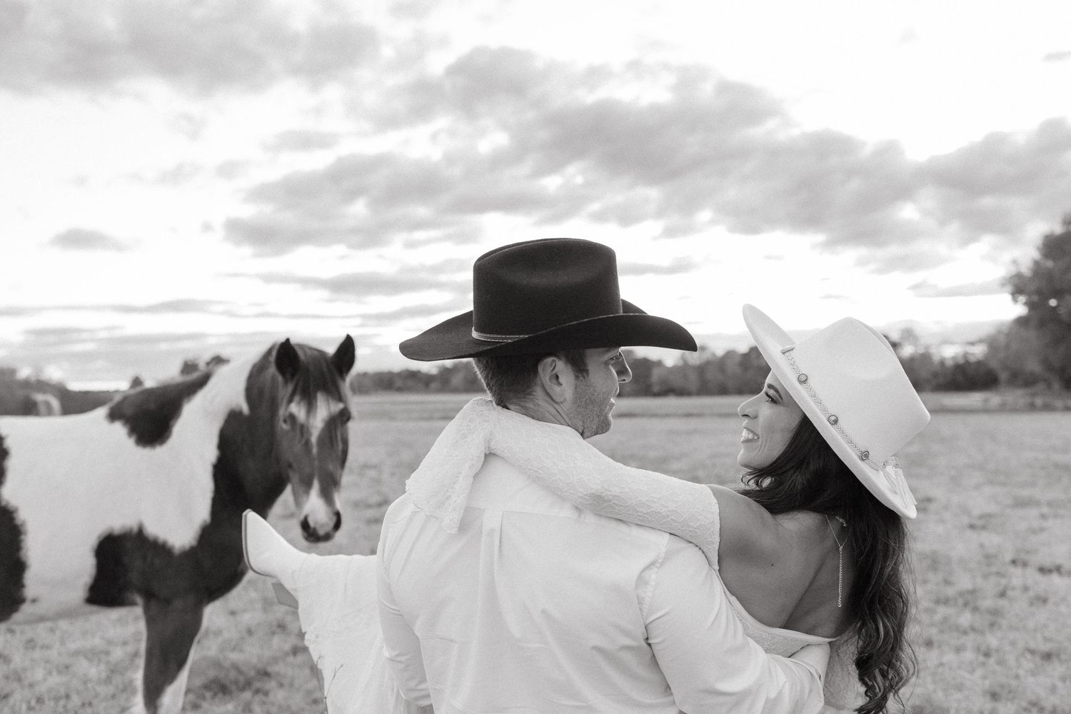 Black and white photo of couple in cowboy hats facing each other with paint horse between them.