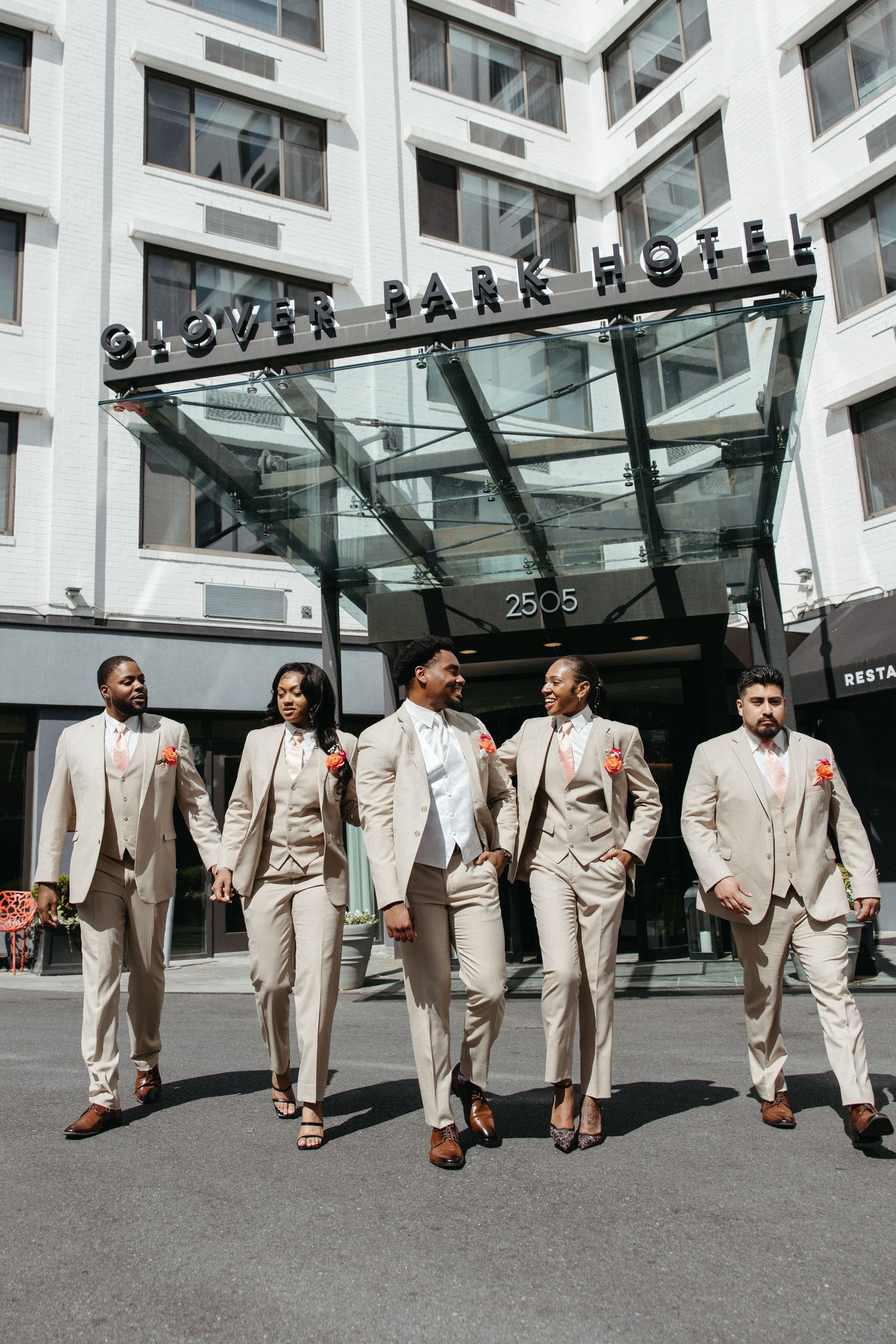 Wedding party in matching beige suits with coral boutonnieres walking confidently outside Glover Park Hotel.