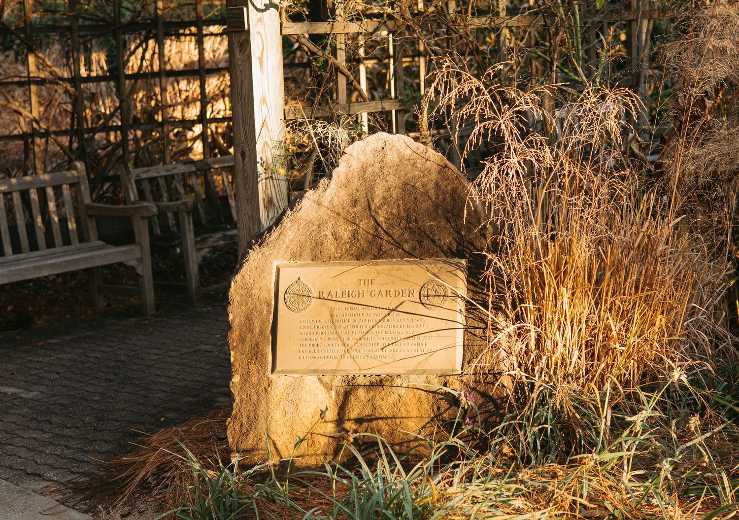 Rustic stone garden marker bathed in warm golden sunlight surrounded by ornamental grasses.