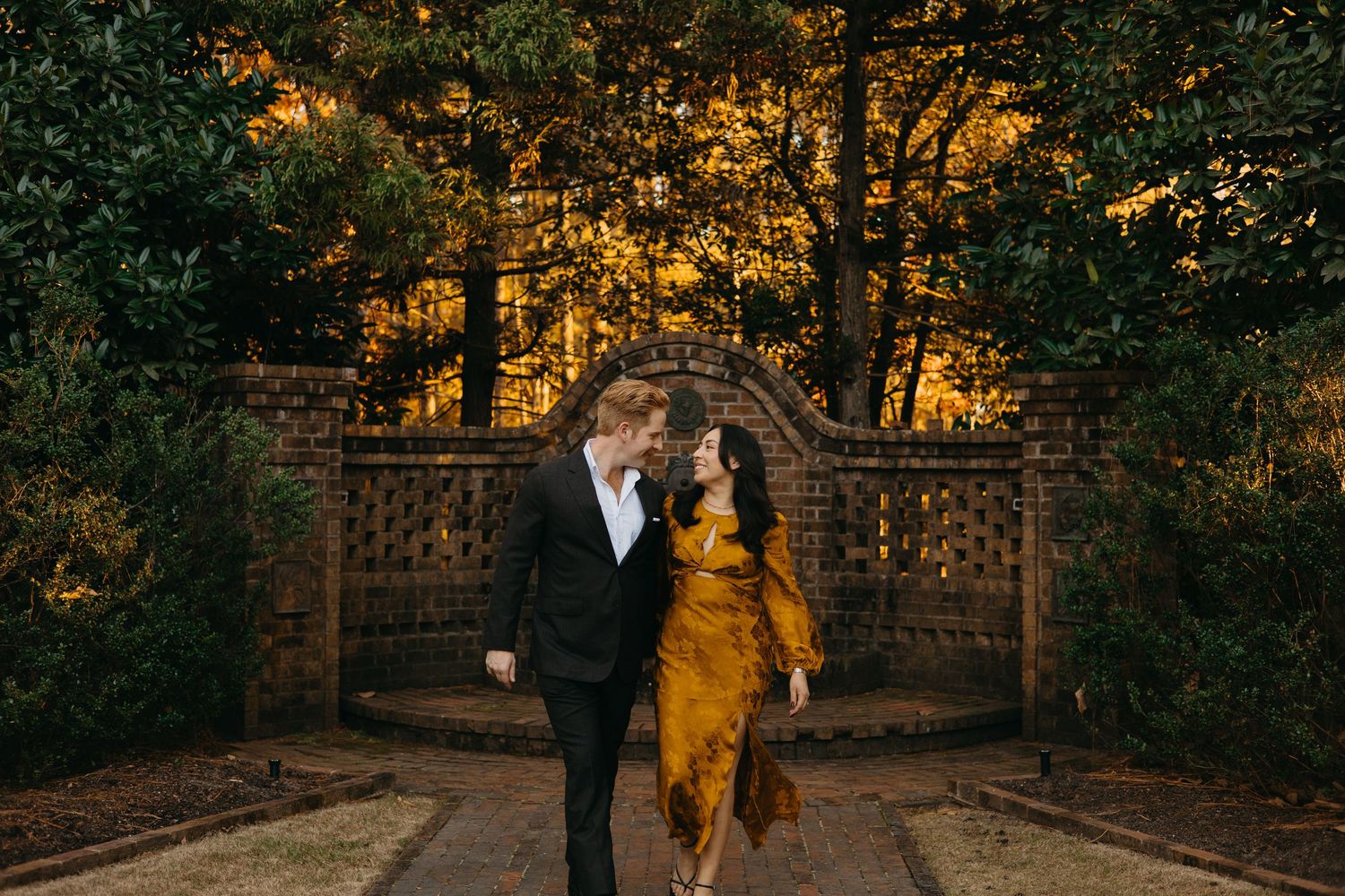 Couple dancing together in front of an ornate garden gate illuminated by warm golden light.