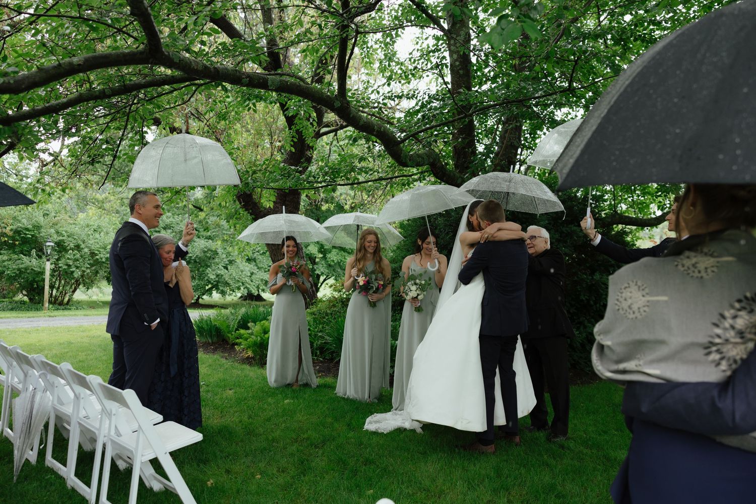 Bride and groom share first kiss at outdoor garden wedding ceremony while guests hold umbrellas.