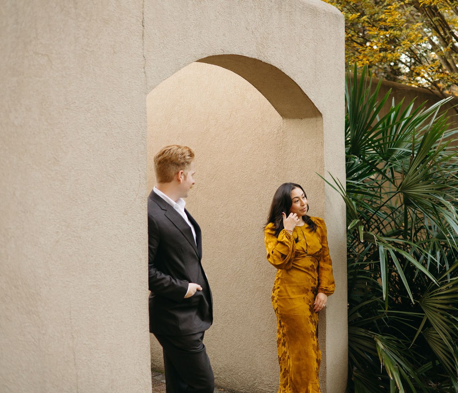 Couple sharing a playful moment under a stucco archway with tropical palms in the background.