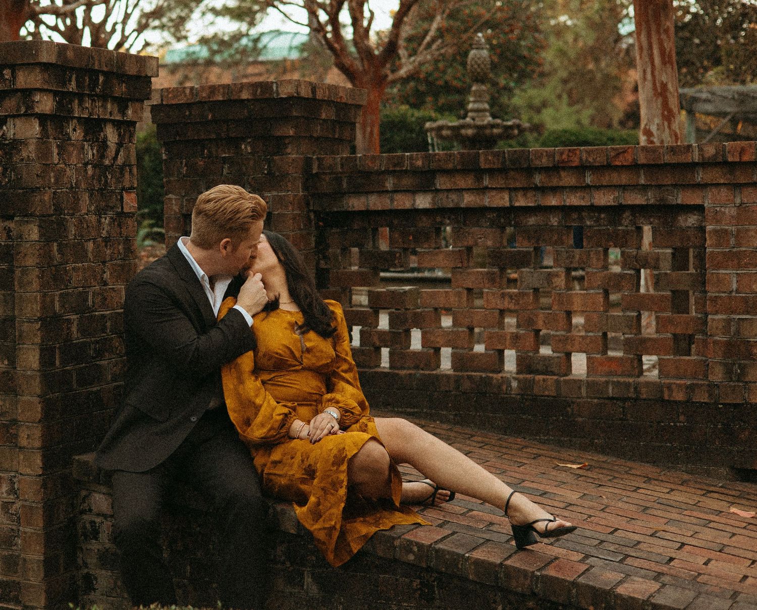 Couple sharing a romantic kiss on a brick wall surrounded by autumn foliage during an engagement session.
