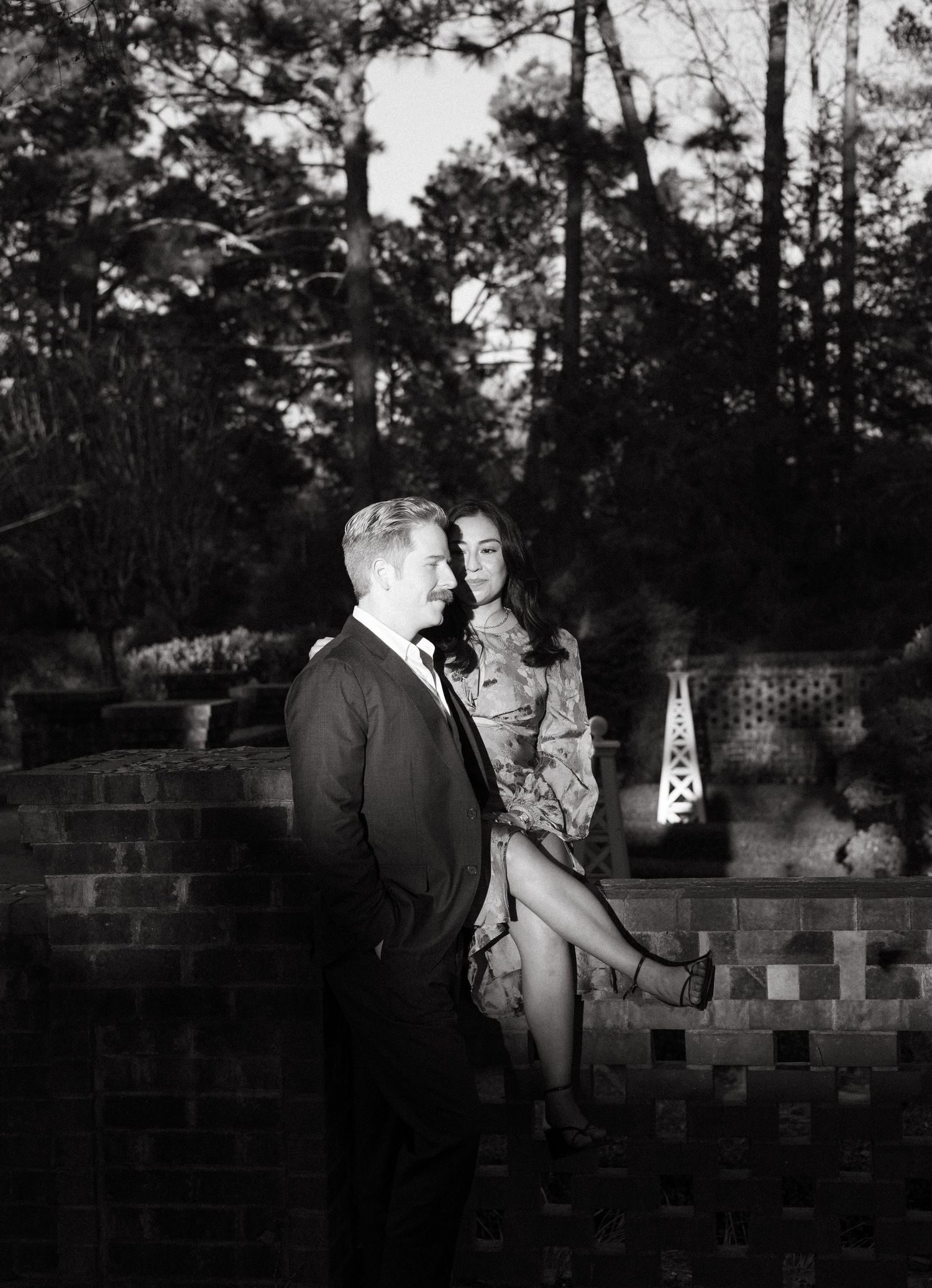 Black and white romantic portrait of a couple on a brick wall in a garden setting.