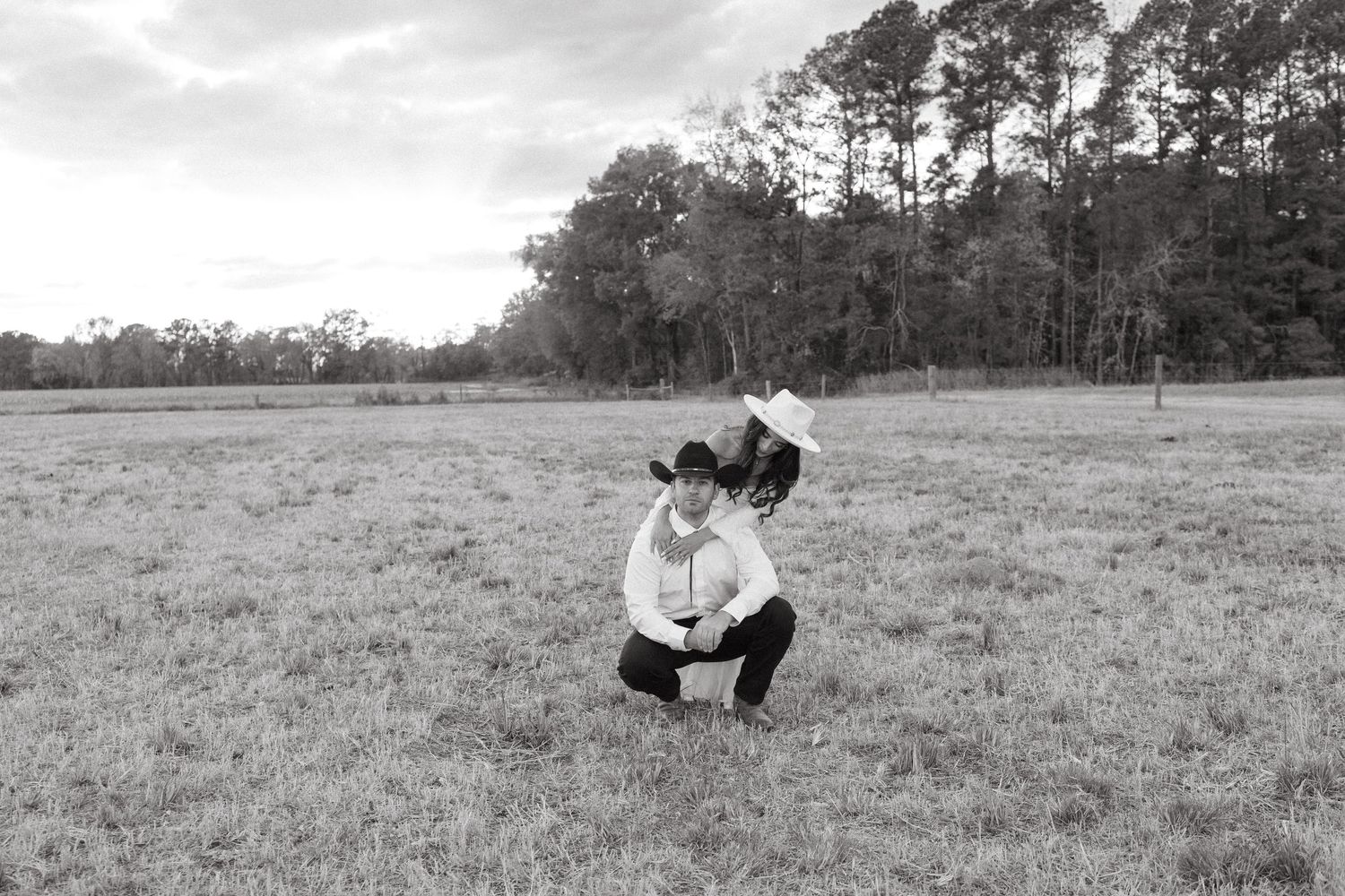 Black and white photo of a couple in cowboy hats sharing an intimate moment in a grassy field.