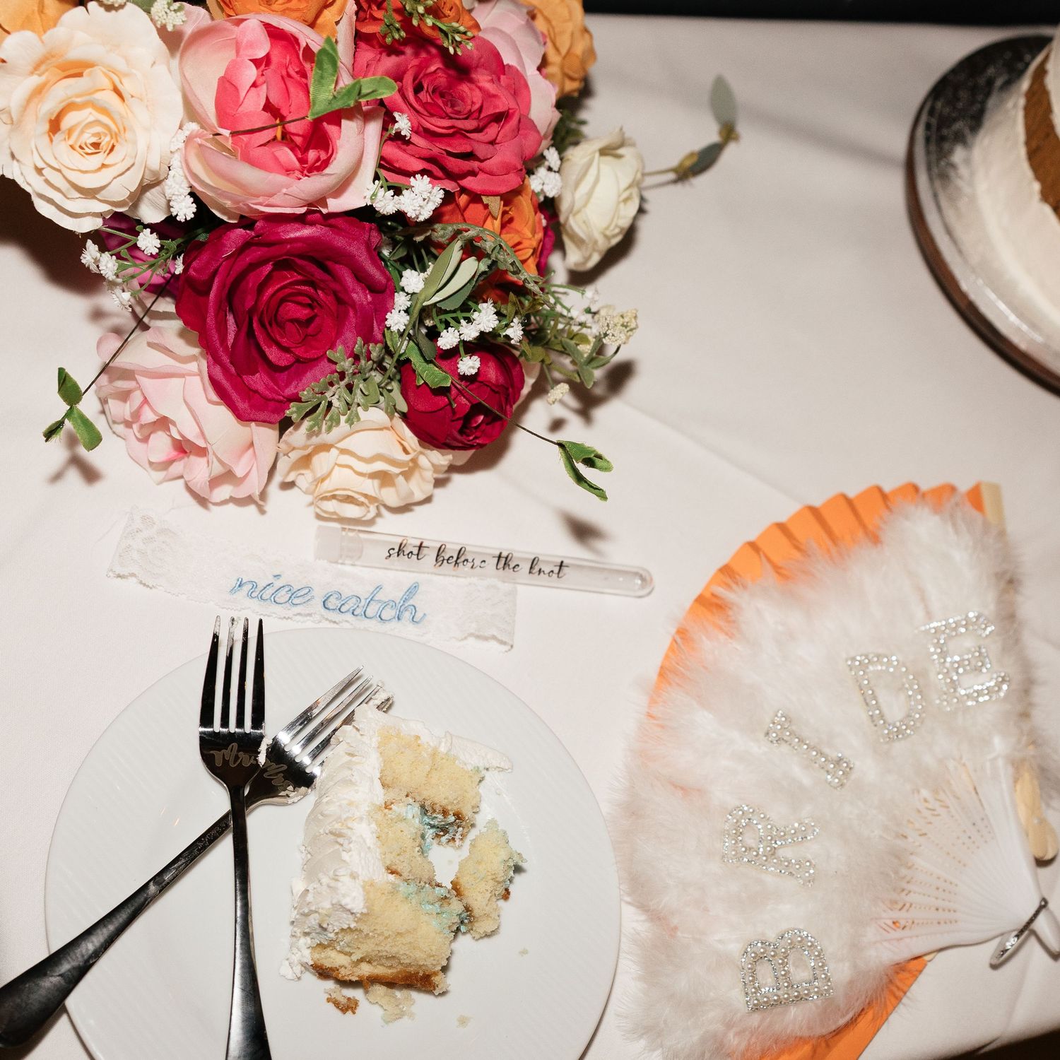 Colorful wedding reception table with pink roses bouquet, cake slice, fork, and decorative fan centerpiece.