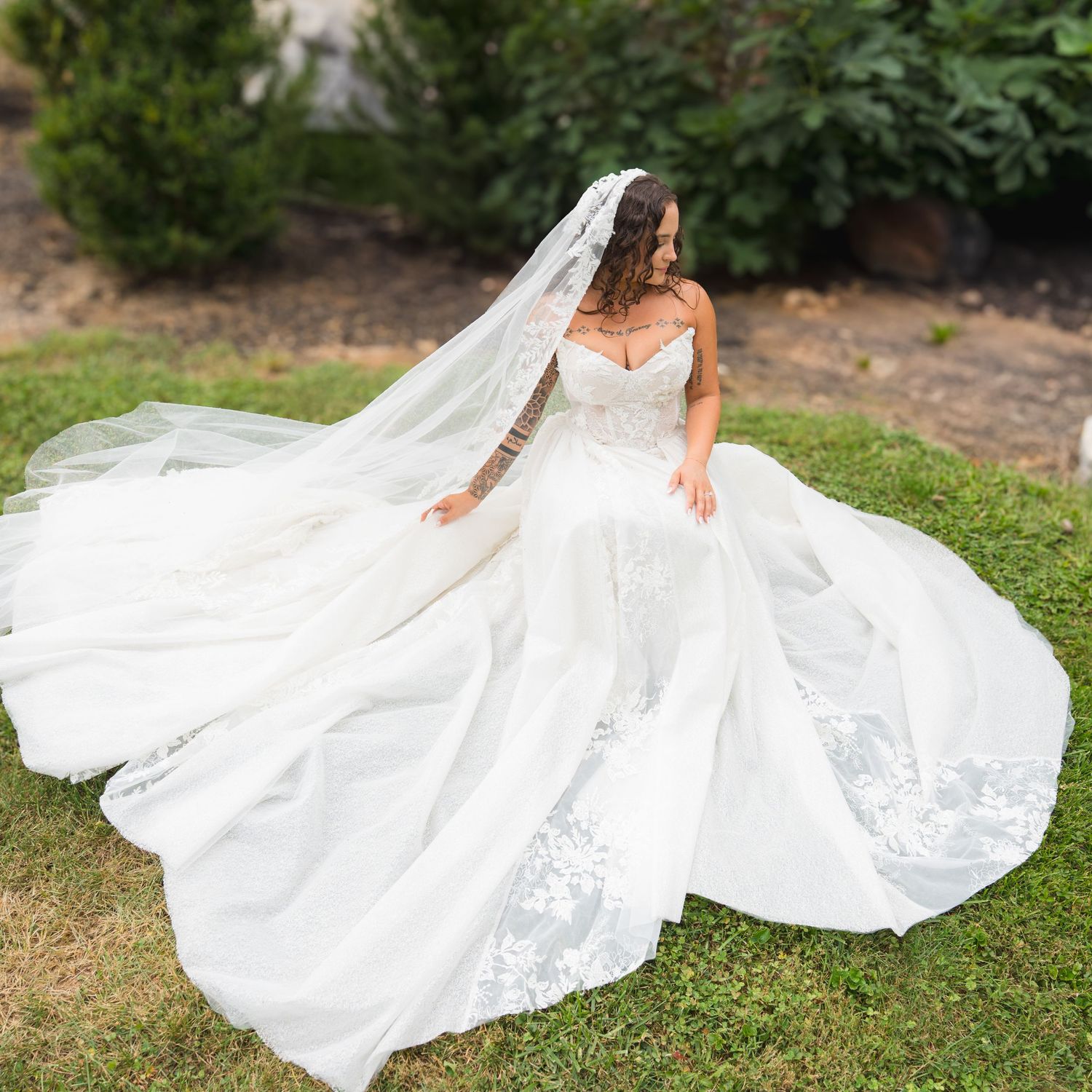 Bride in elegant lace wedding gown with long veil posing in garden.