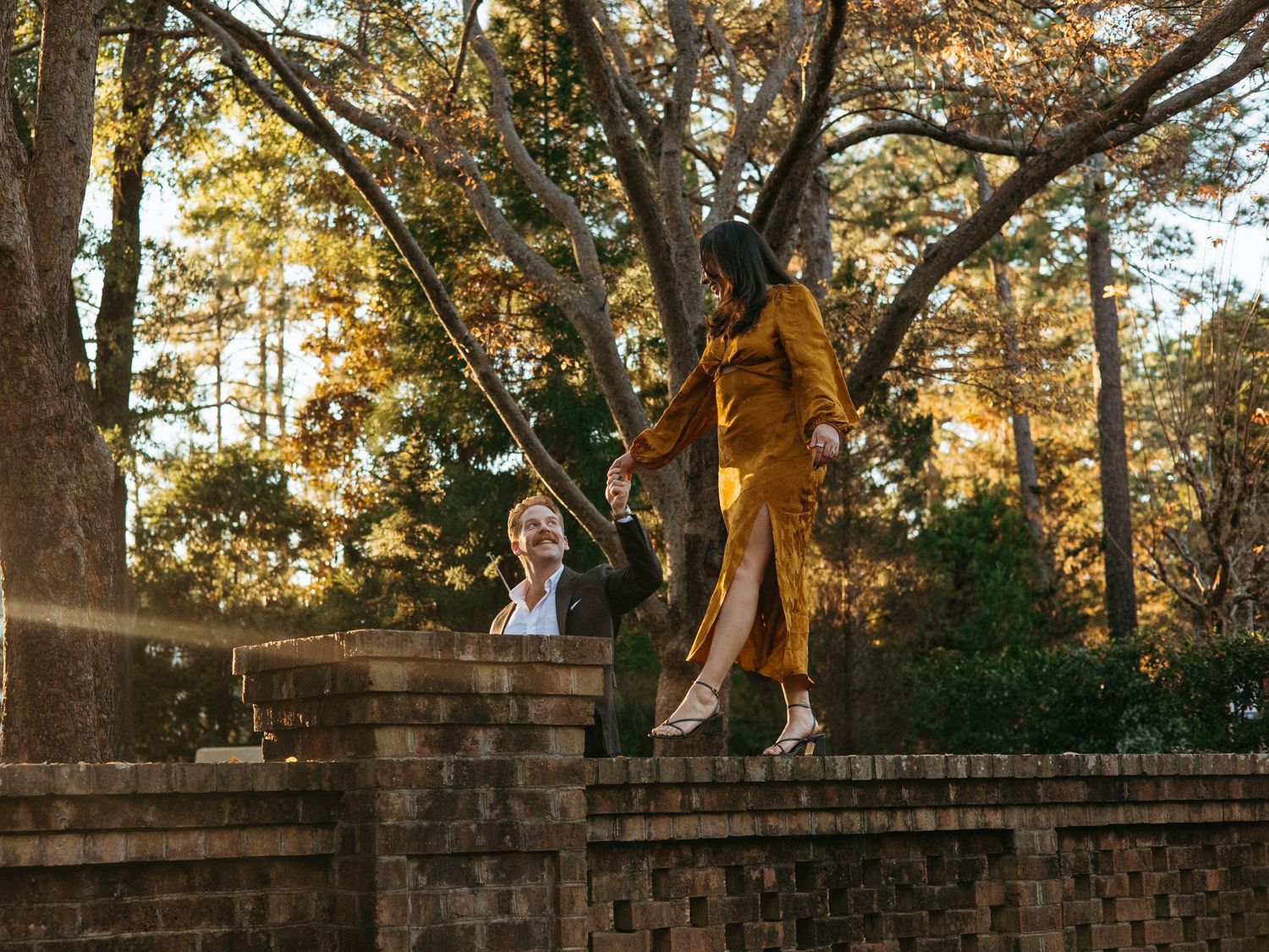 Woman balancing on a brick garden wall holding hands with her partner below.
