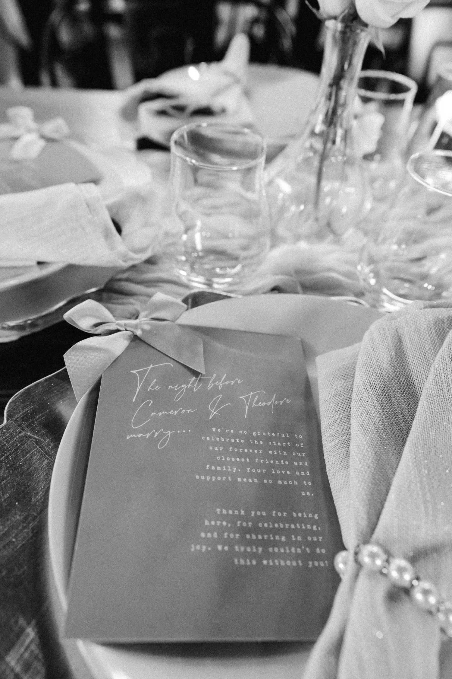 Black and white close-up of elegant wedding dinner menu card tied with ribbon on table setting.