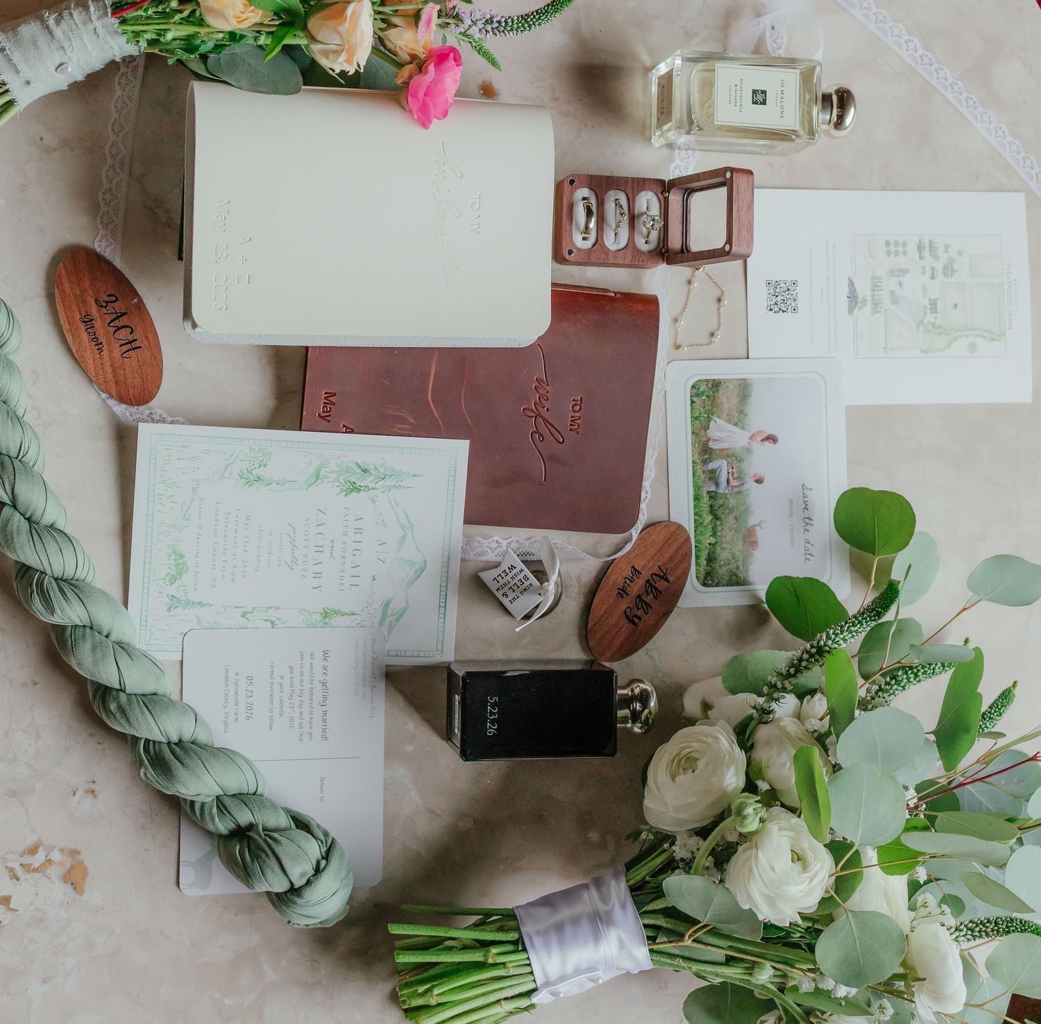 Flat lay of wedding stationery, florals, perfume, and accessories arranged on a surface.