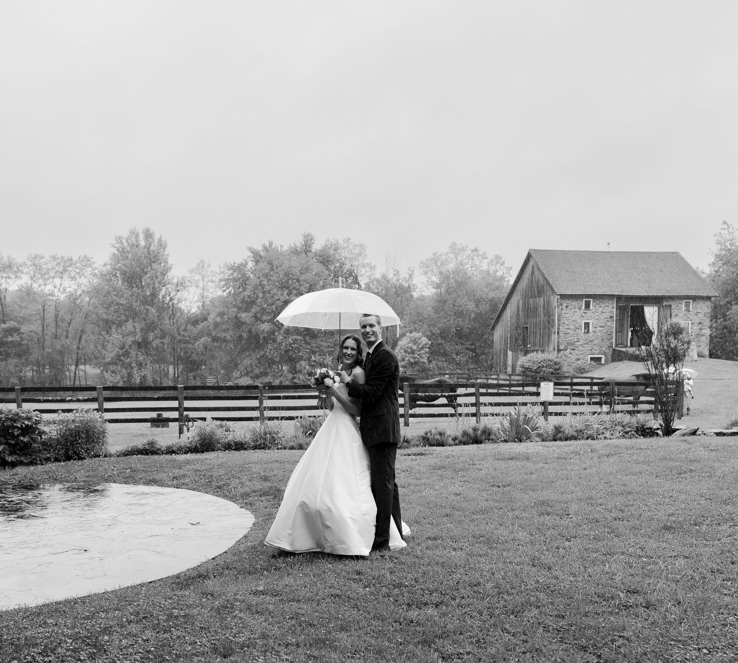 Bride and groom share a romantic moment under a clear umbrella on a rainy wedding day.