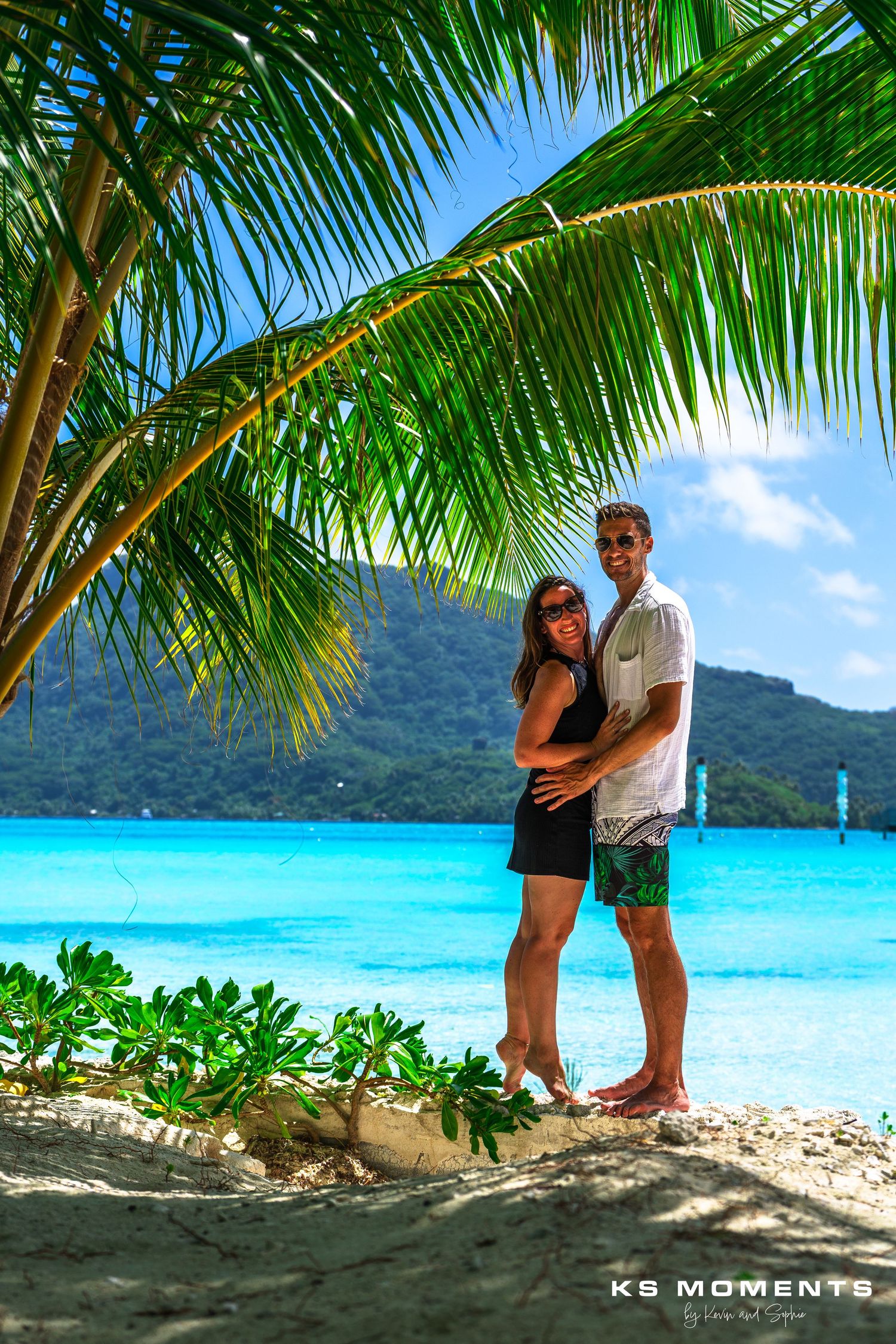 Photo d'un couple sur une plage avec des palmiers et de l'eau turquoise en arrière plan