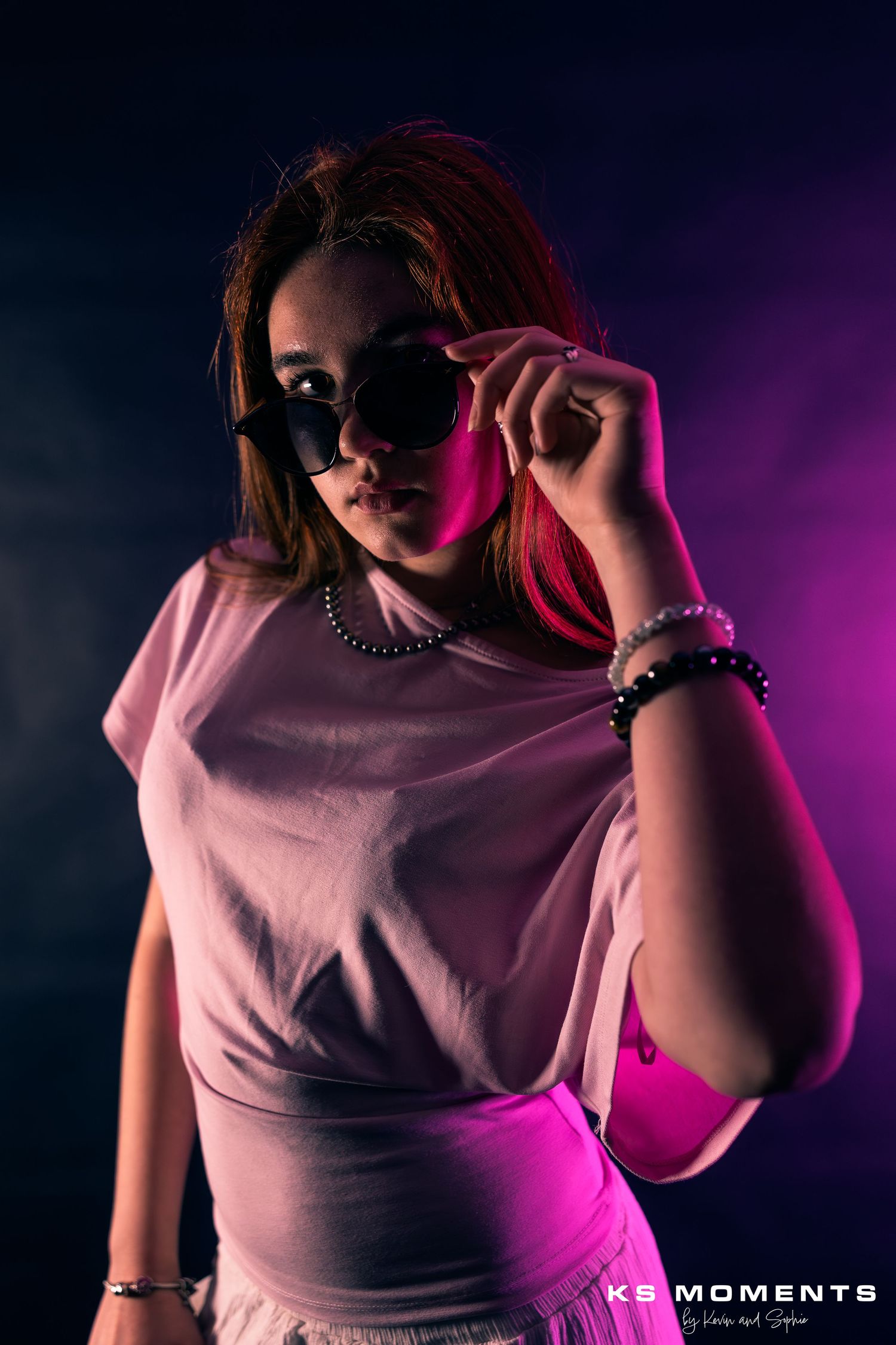 Photo d'une jeune fille dans un studio photo avec un fond noir et des lumières de couleur rose violet