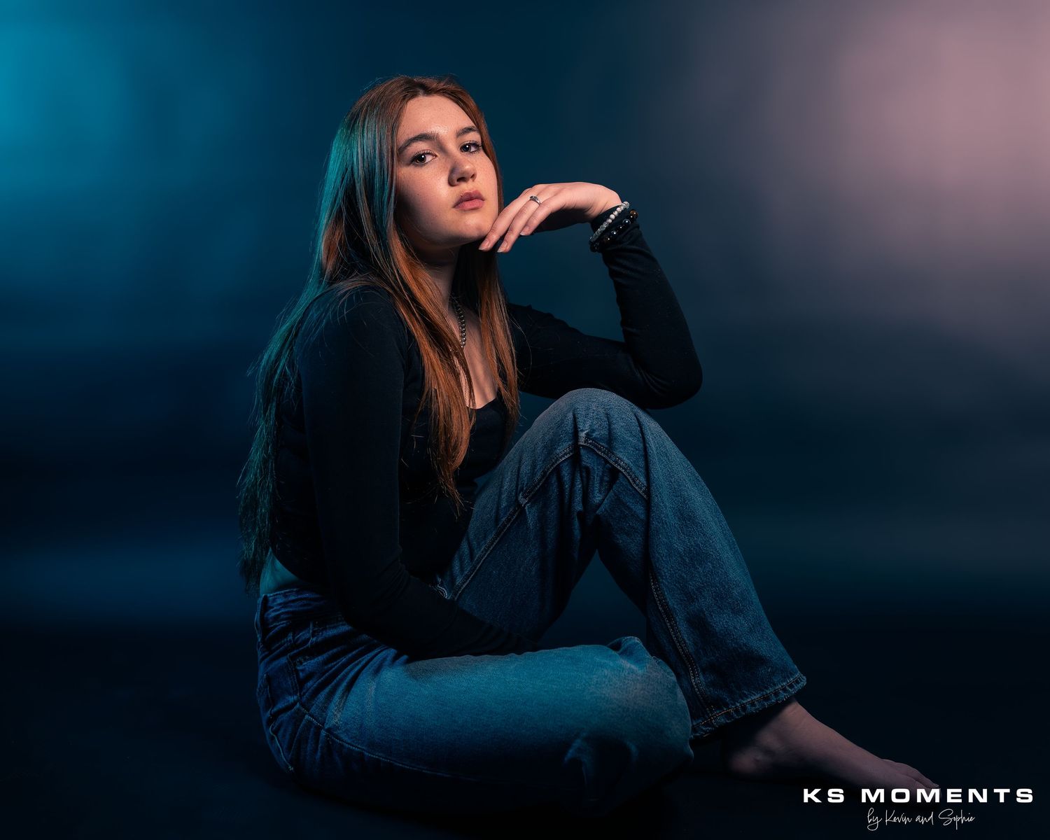 Photo d'une jeune fille assise dans un studio photo avec un fond noir et des lumières de couleur bleue