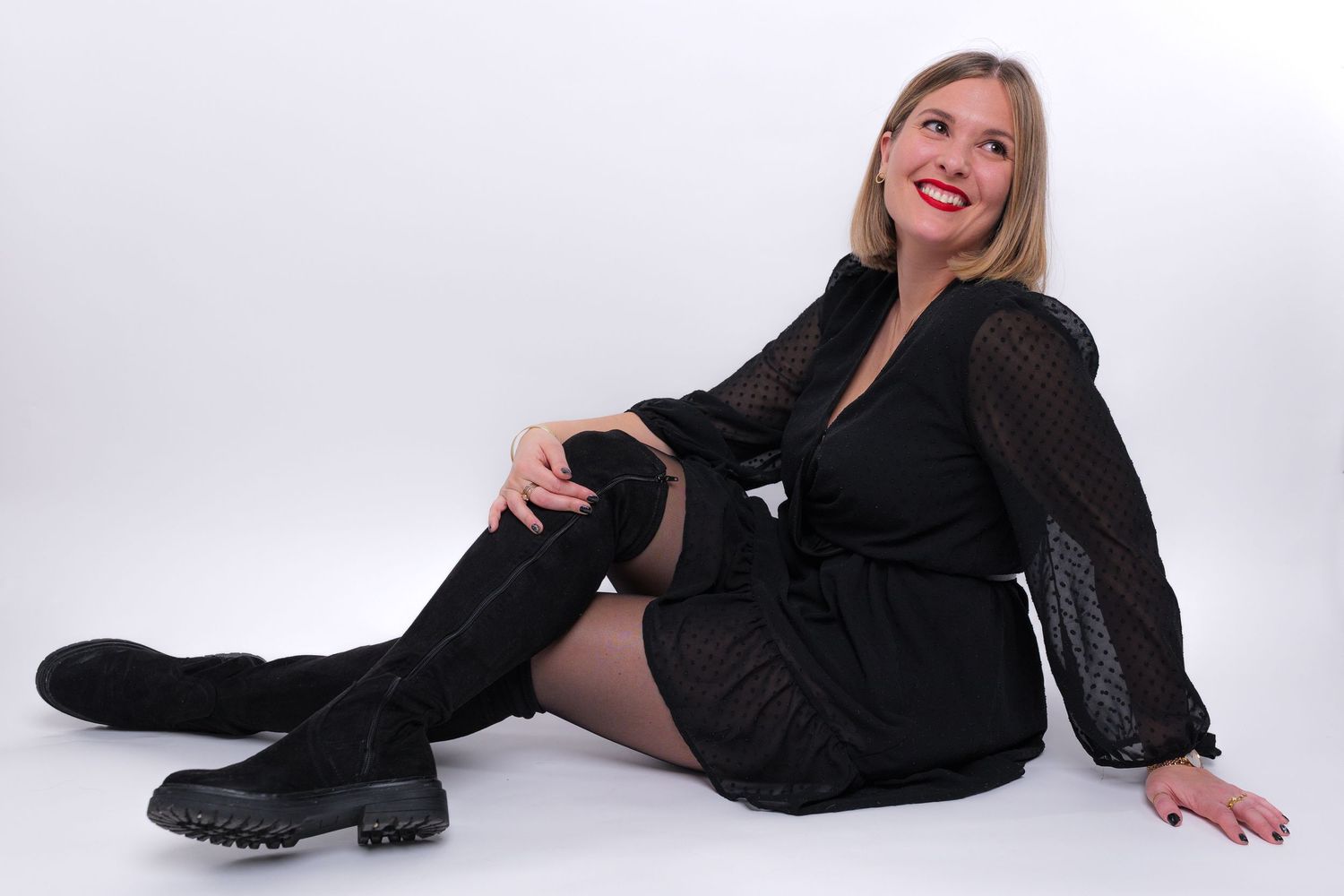 Photo d'une femme souriante assise par terre dans un studio photo avec un fond blanc