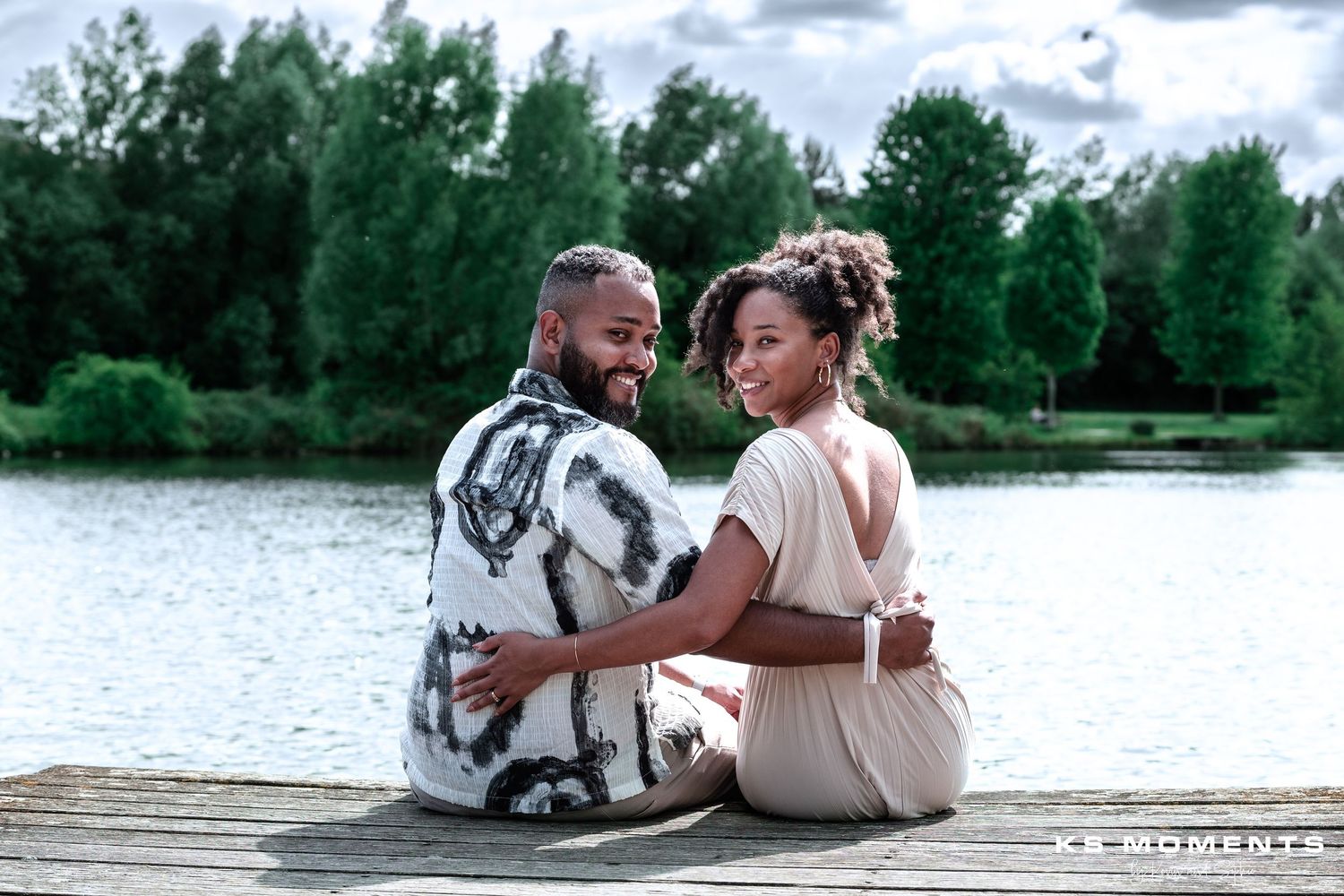 Photo d'un couple assis au bord de l'eau et tournant la tête pour nous regarder