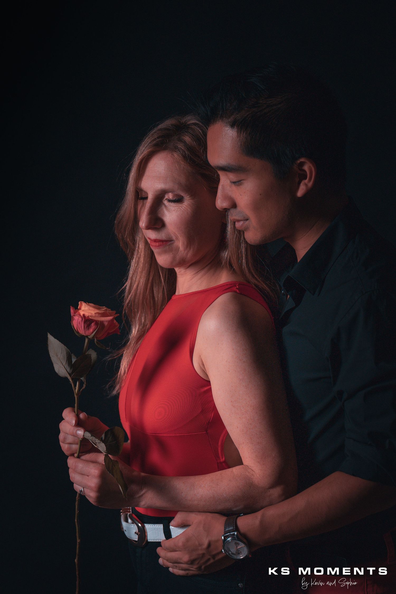 Photo d'un couple avec les yeux fermés et une fleur dans la main dans un studio photo avec un fond noir