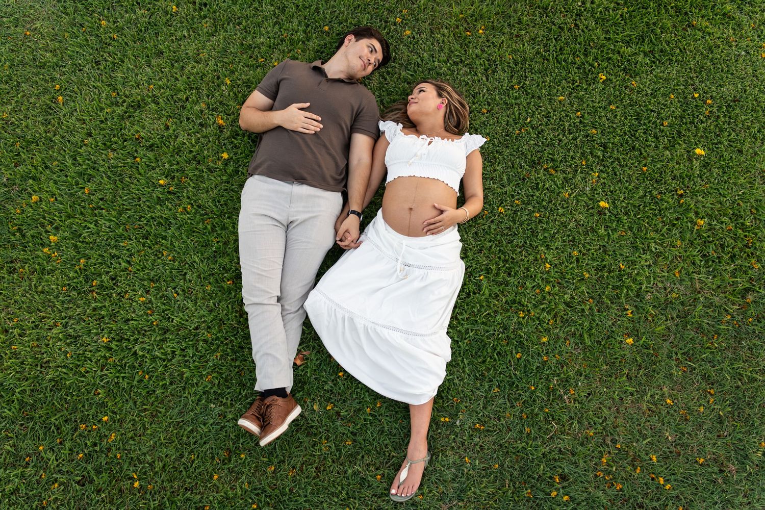 Couple lying on green grass, pregnant woman in white dress and man in brown shirt.