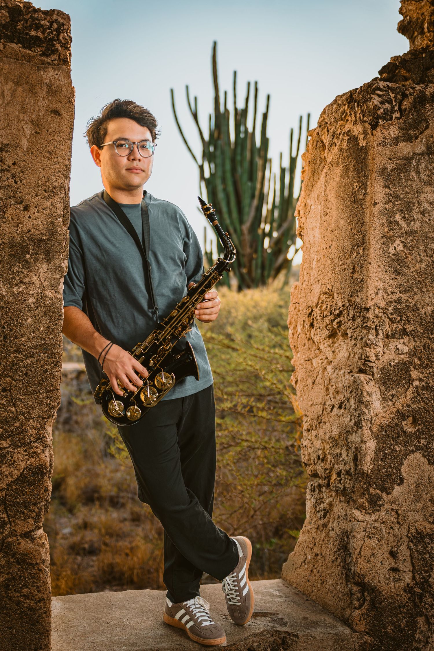 Musician holding a saxophone among rugged rock formations and a cactus in Aruba, personal branding portrait