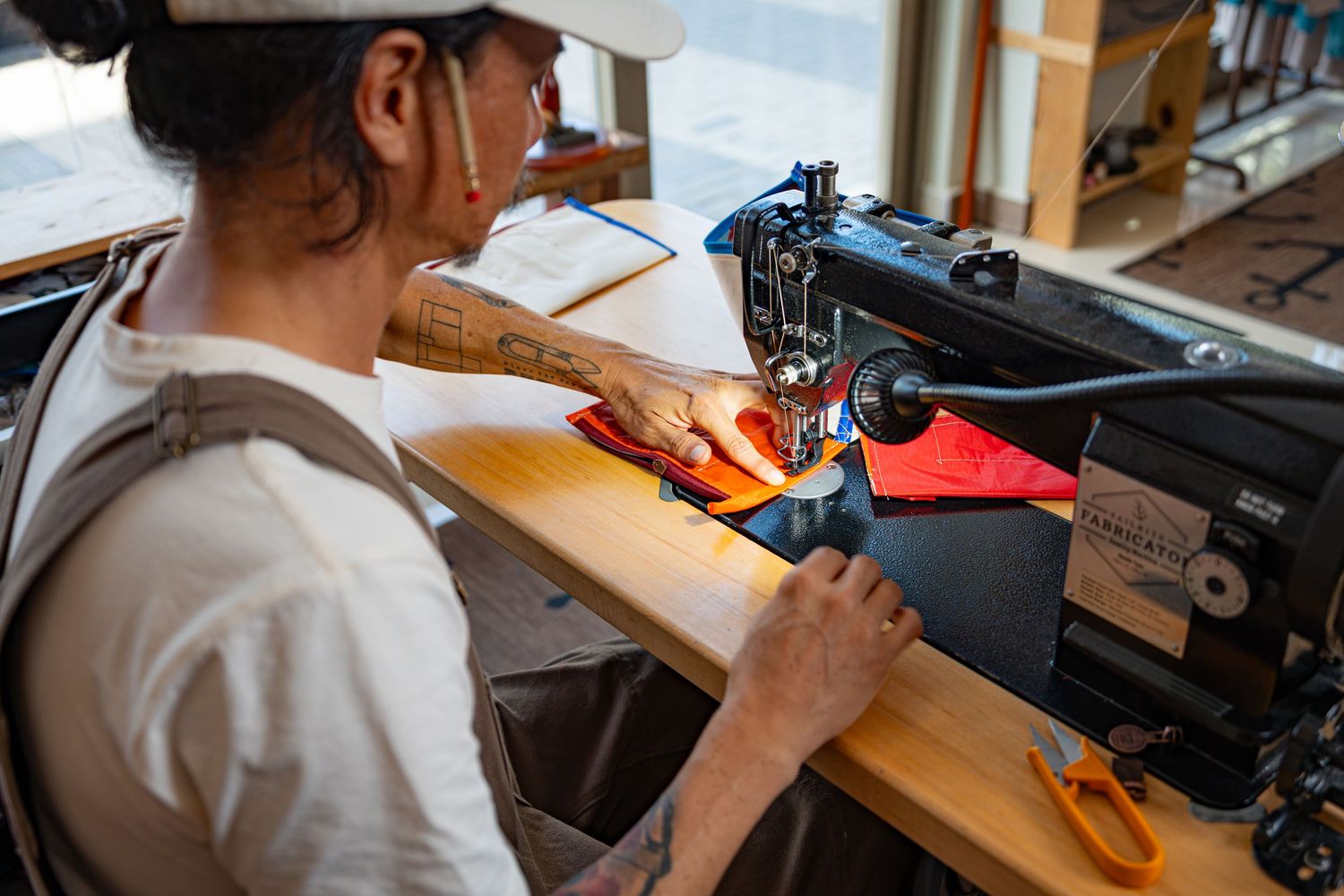 Craftsperson using an industrial sewing machine to stitch red fabric in a workshop.