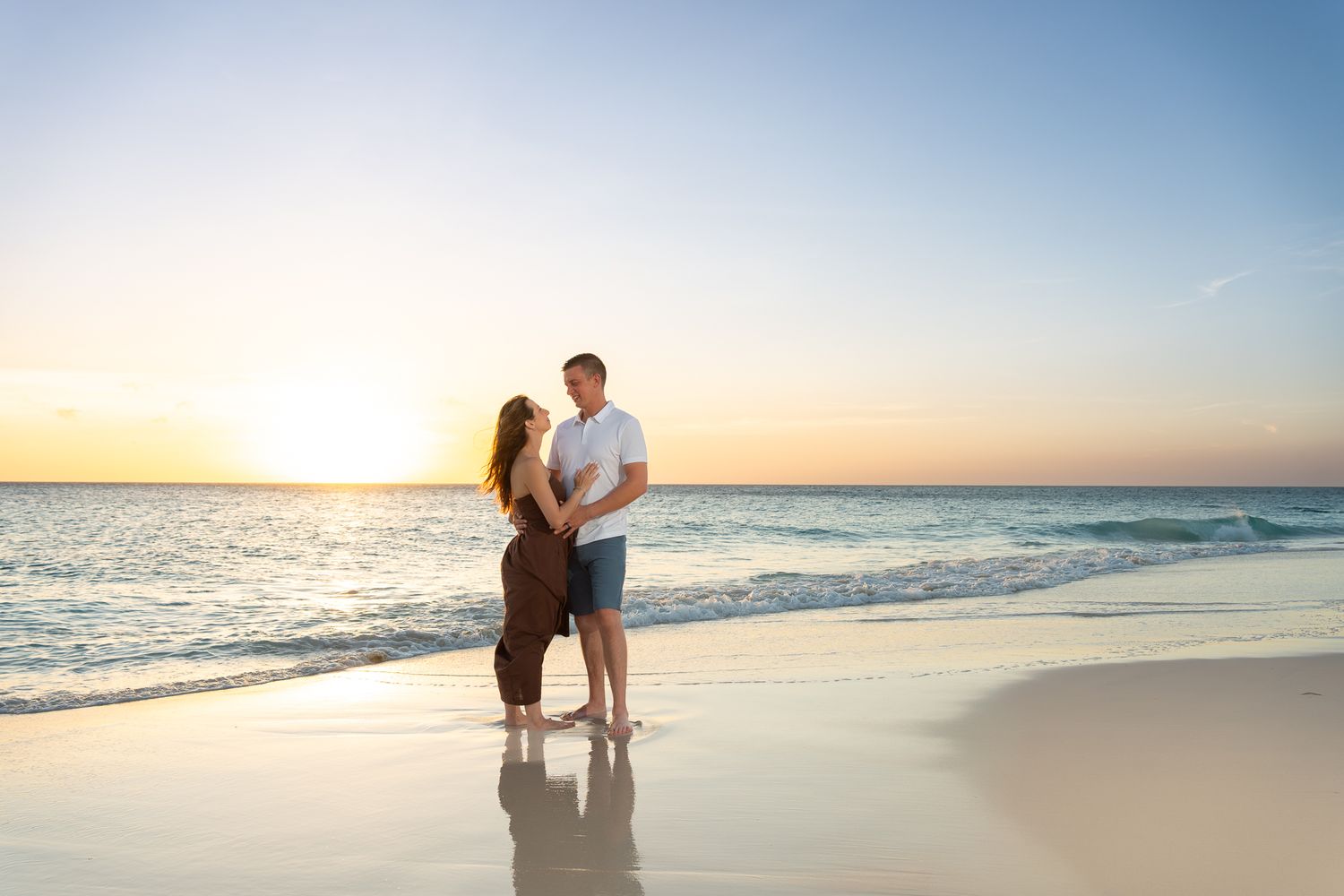 Romantic couple embracing on a pristine beach at stunning golden sunset with turquoise water.