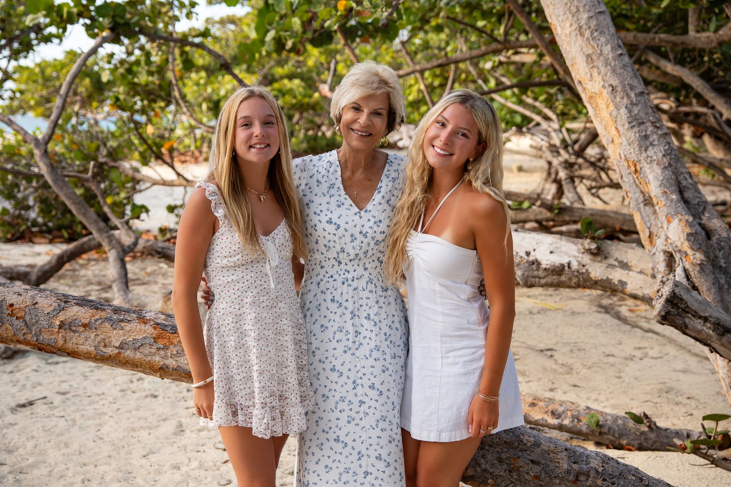 Mother and two daughters in white dresses on an Aruba beach, framed by sea grape trees at golden hour.