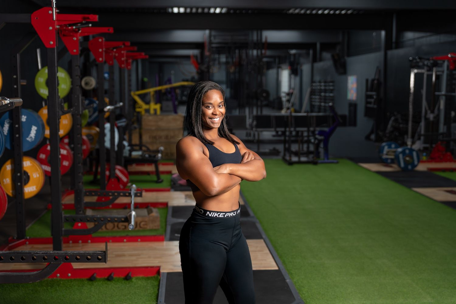 Female personal trainer standing with arms crossed in a fully equipped gym, personal branding portrait in Aruba