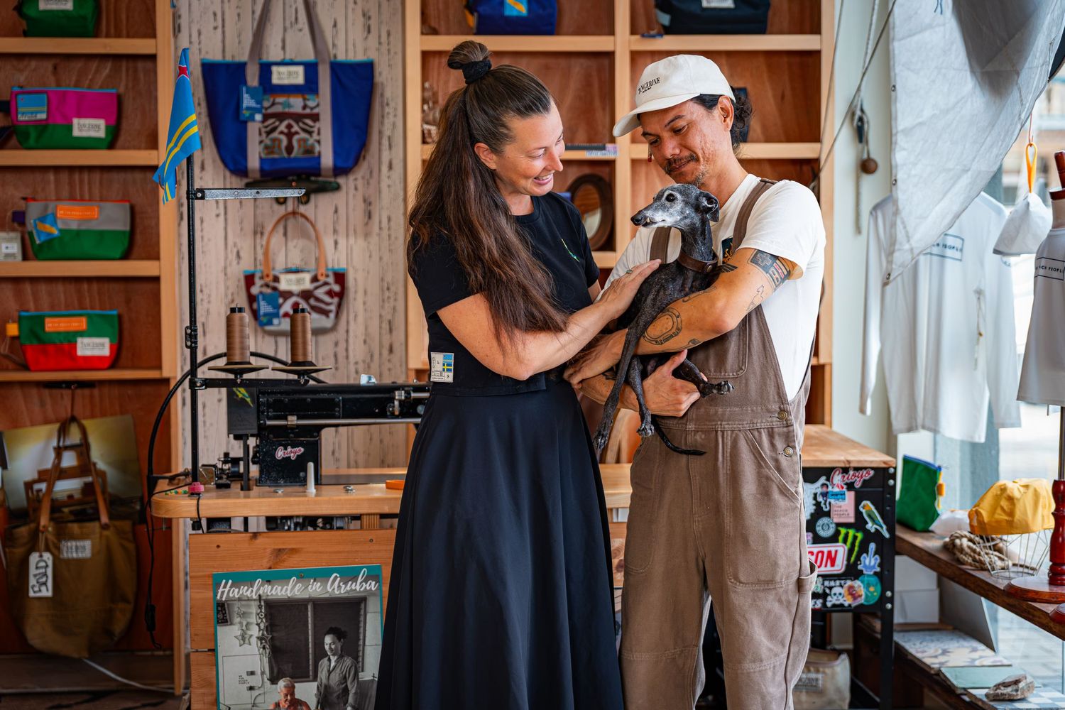 Two people smiling and petting a small dog inside a colorful artisan craft shop.