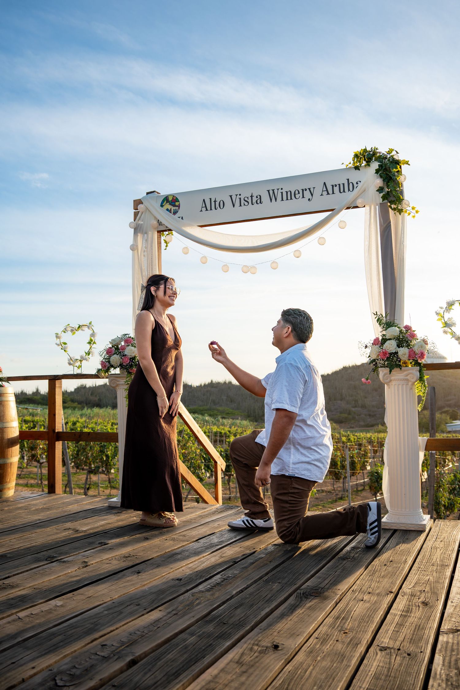 Man proposing on one knee under floral archway at Alto Vista Winery Aruba at dusk.