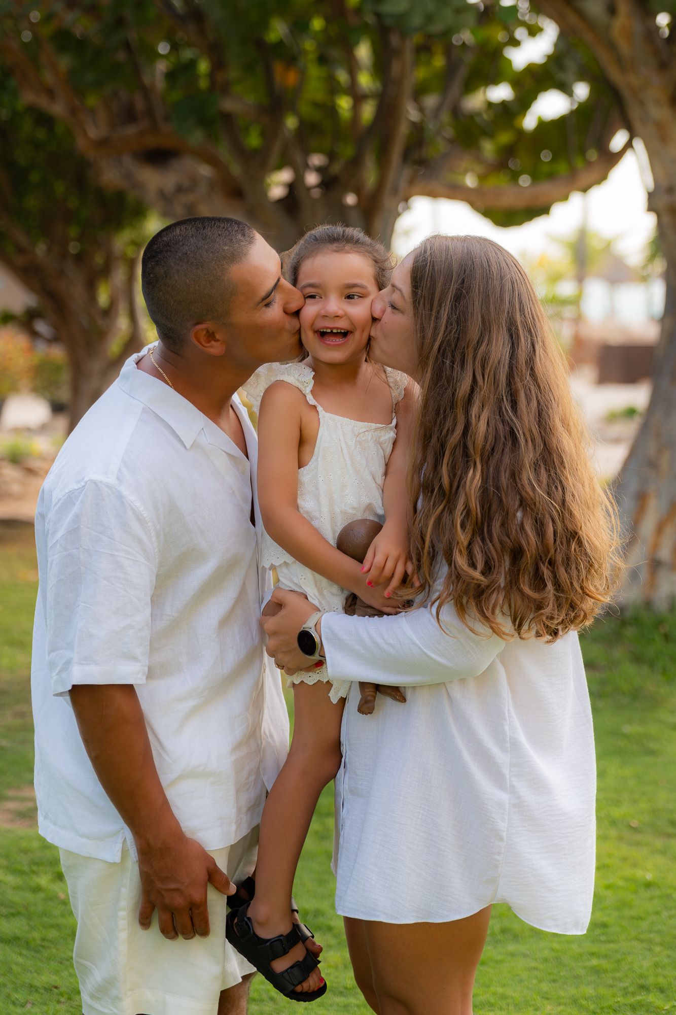 Family of three in white outfits sharing a hug during an Aruba family photoshoot at golden hour.