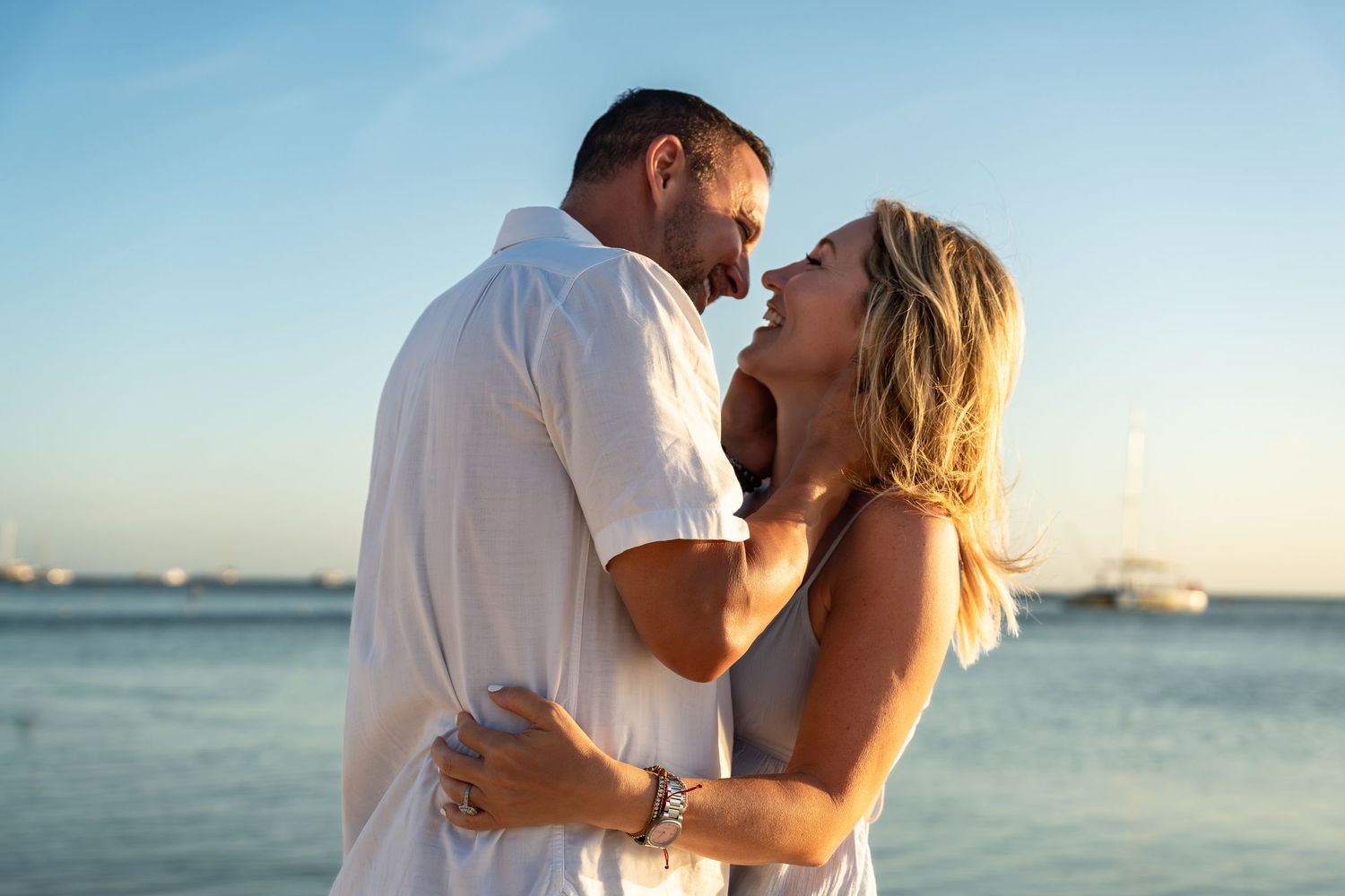 Couple embracing and smiling at each other on a beautiful beach at sunset.