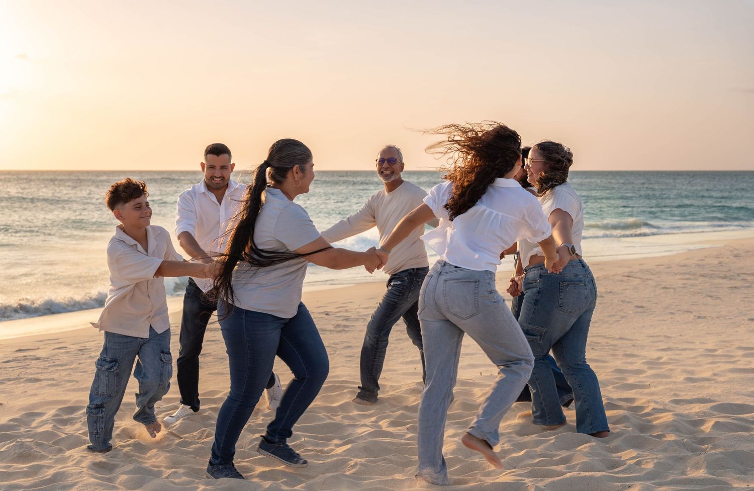 Joyful extended family dancing together in a circle on Eagle Beach Aruba at golden sunset hour – Jonathan Geerman Studio