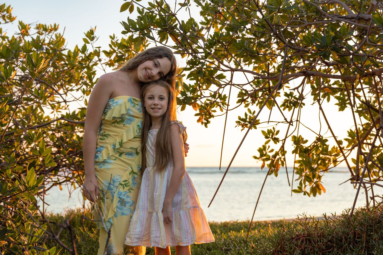 Mother and daughter embracing under tropical trees near the calm ocean in Aruba – Jonathan Geerman Studio