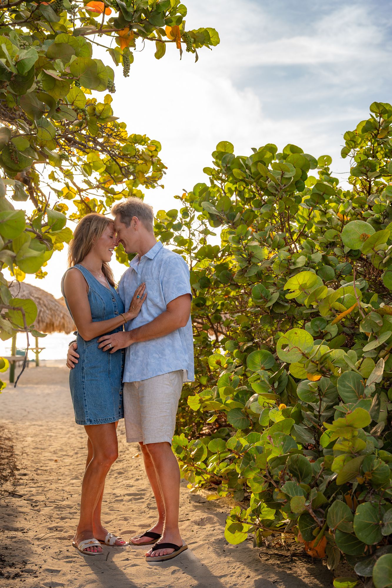 Couple sharing a tender nose-to-nose moment surrounded by lush green tropical foliage on a beach.