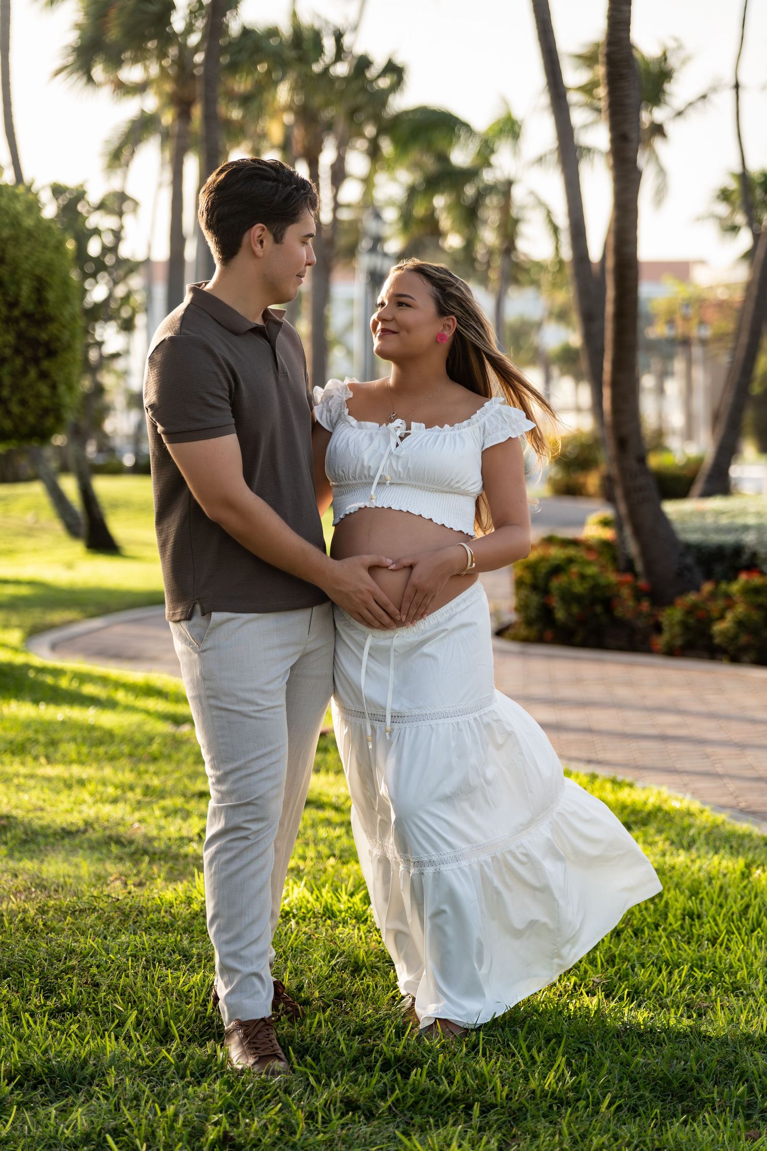 Expectant couple in a palm-lined Aruba garden during a maternity photoshoot, holding the baby bump.
