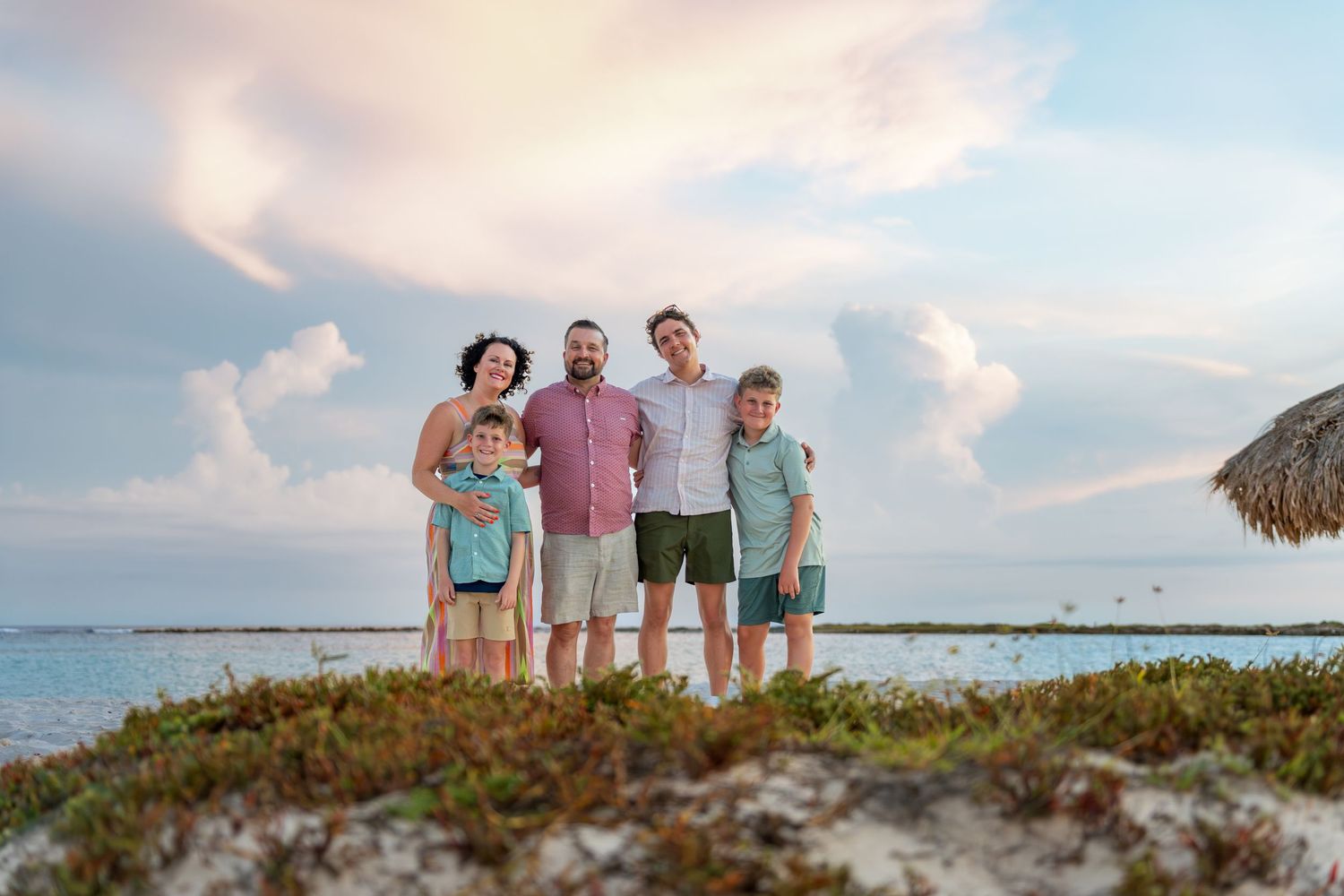 Family of five posing on an Aruba beach at dusk with a calm ocean in the background – Jonathan Geerman Studio