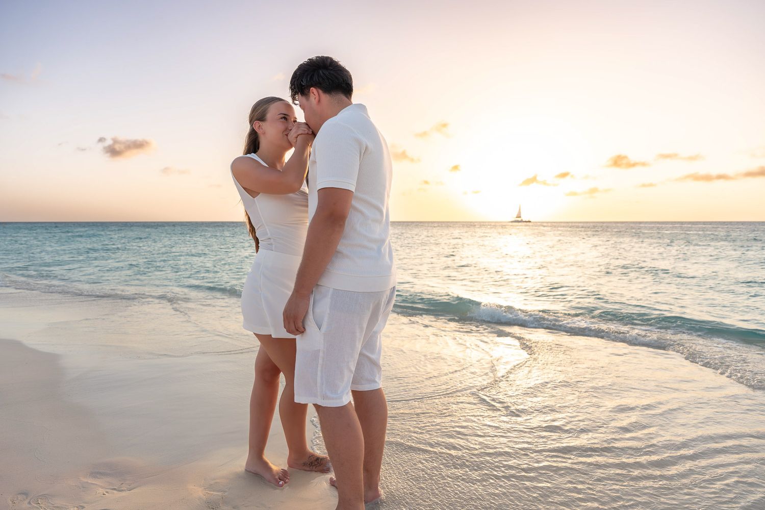 Couple in white outfits holding each other at the water's edge on an Aruba beach at sunset, romantic couples photoshoot