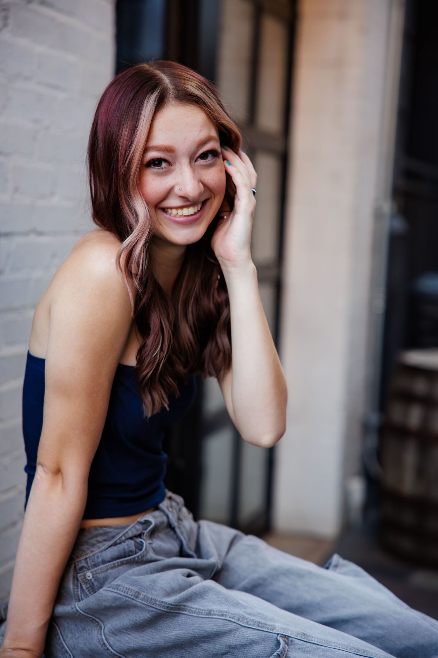 Smiling young woman in blue crop top and jeans sitting outdoors  for Parker CO Senior photos
