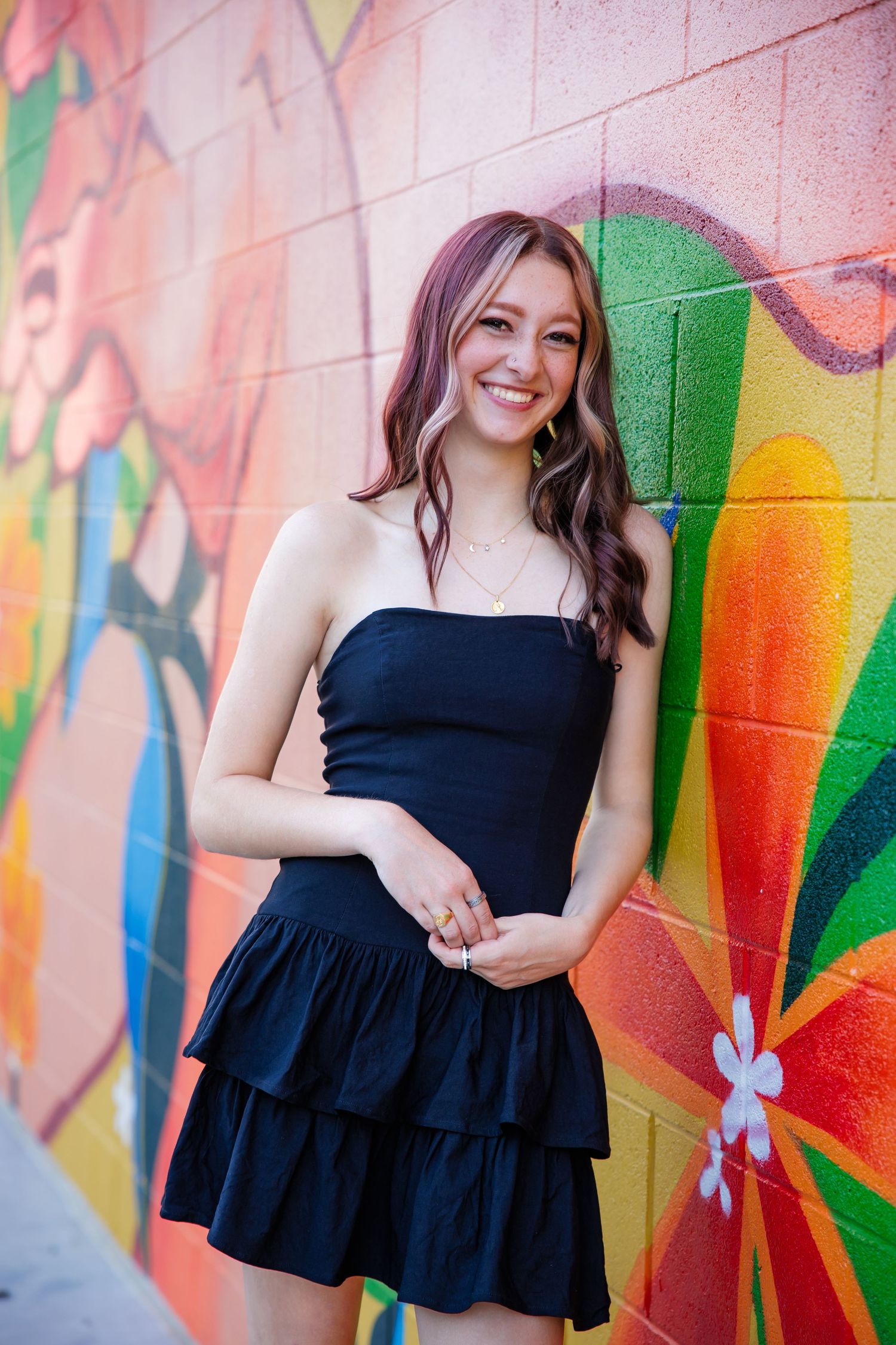 Smiling teen girl in black strapless dress posing in front of colorful graffiti mural wall for Denver Colorado Senior pictures