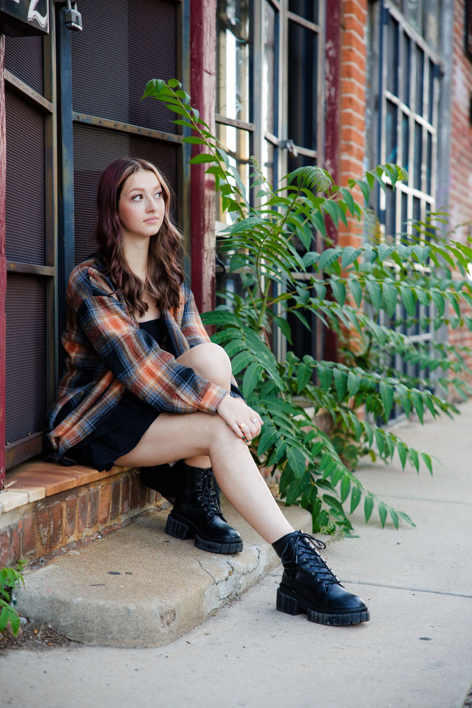 Young woman in plaid shirt and boots sitting on steps near brick building  for Parker CO Creative Senior photos