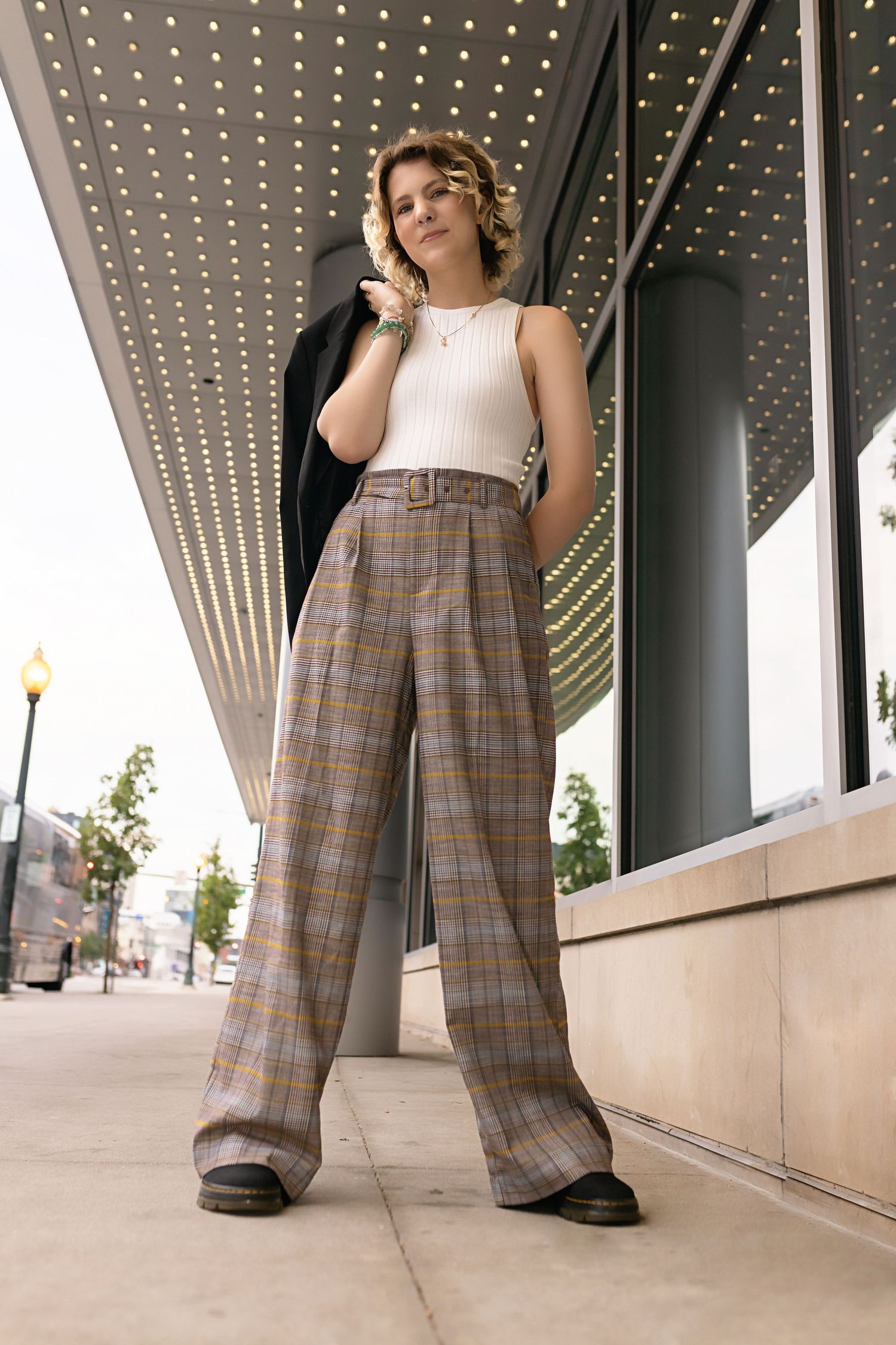 Stylish teen in plaid wide-leg trousers and white tank top posing under marquee lights. Colorado urban senior images