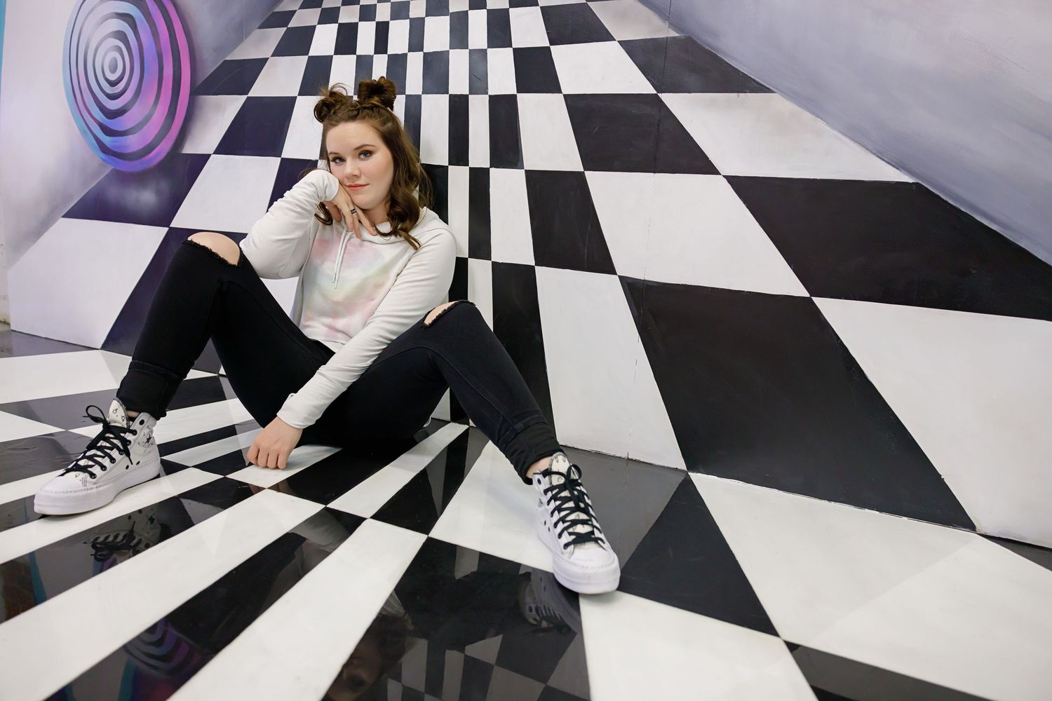 Young woman sitting on a black and white checkered floor in a psychedelic room wearing sneakers and casual outfit  in Downtown Denver