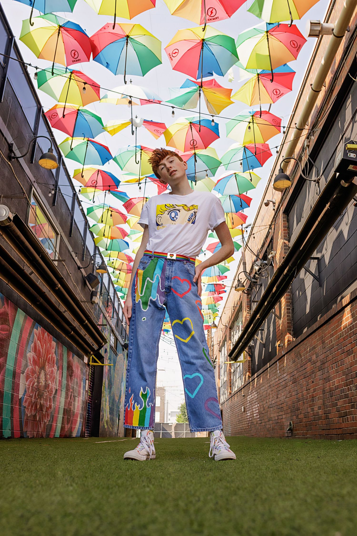 Colorado High School person in painted jeans and graphic tee stands in colorful alley under rainbow umbrellas with graffiti walls in Denver